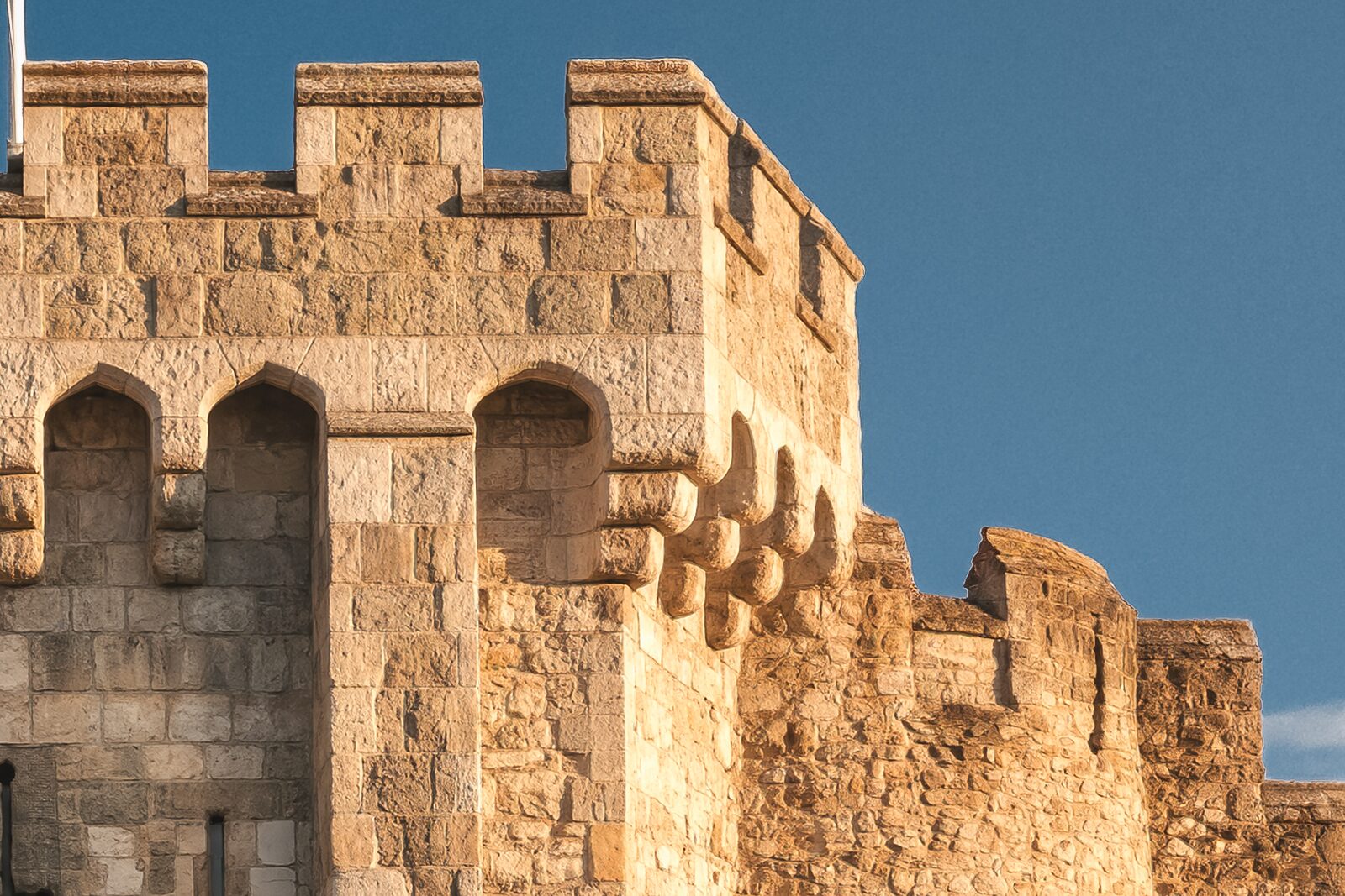 The top right corner of the Bargate shown at full size, the low sun raking across the corbels under the battlements and the flint rubble wall beyond
