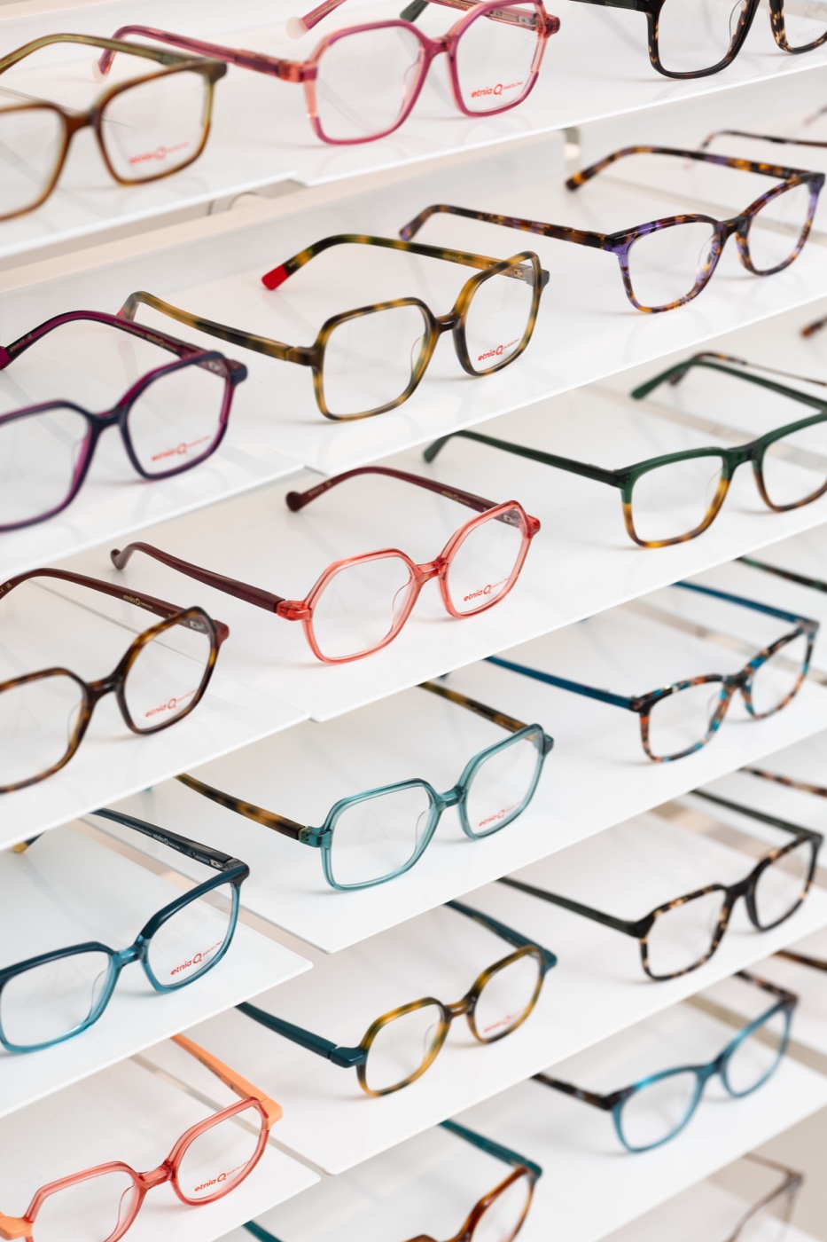 Rows of colourful glasses frames on white shelves in an opticians