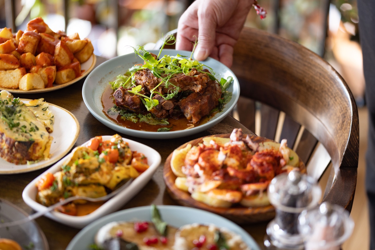 Spanish tapas spread at La Regata Southampton with patatas bravas, tortilla, pulpo a la gallega and slow-cooked ribs being set down on a wooden table, food photography by Ryan Stanikk