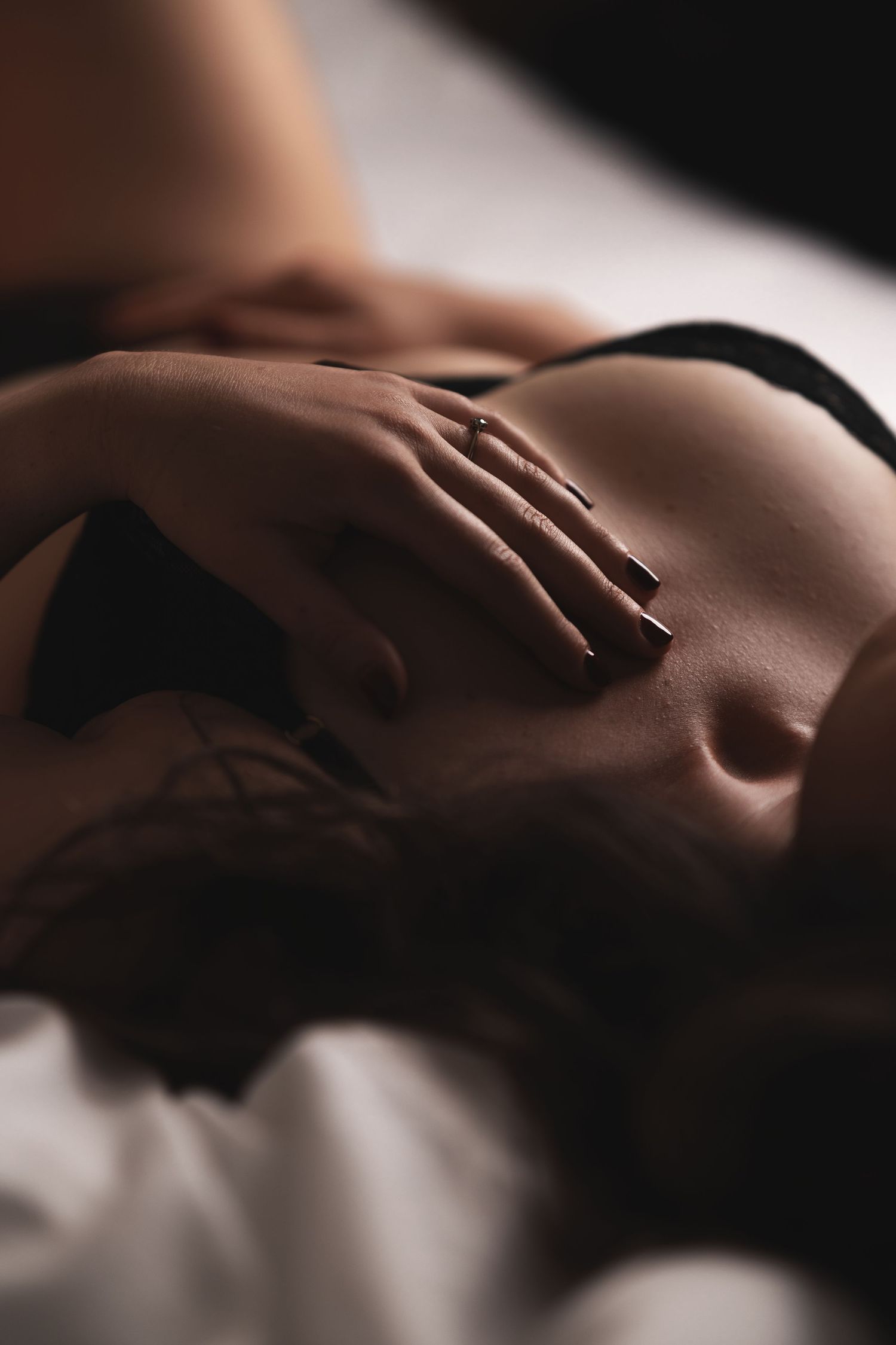 Close-up detail of a woman in black lingerie lying on white sheets with soft natural light, intimate fine art boudoir photography Southampton