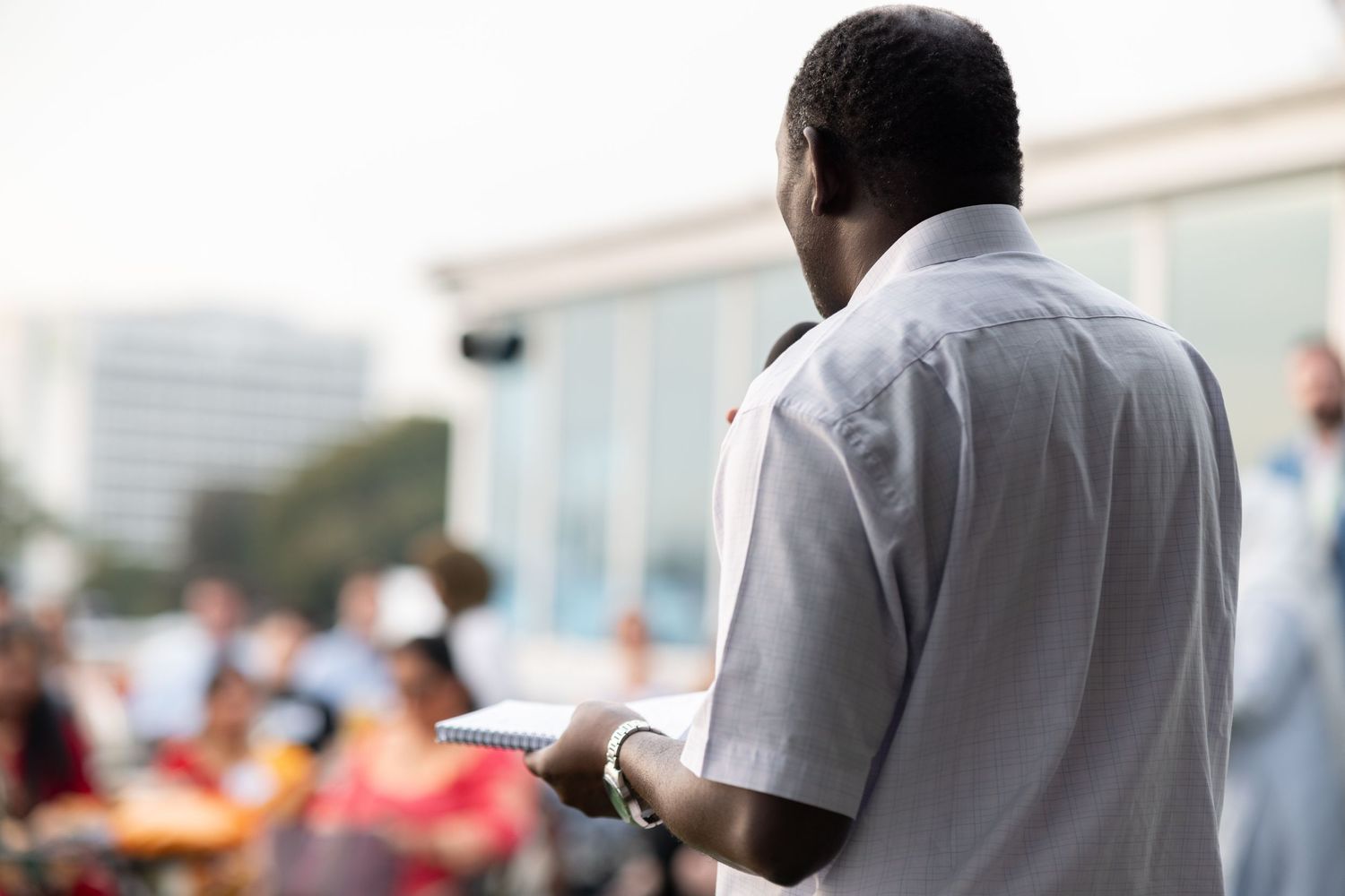 Speaker seen from behind addressing an outdoor audience while holding a notebook, corporate event photography Southampton