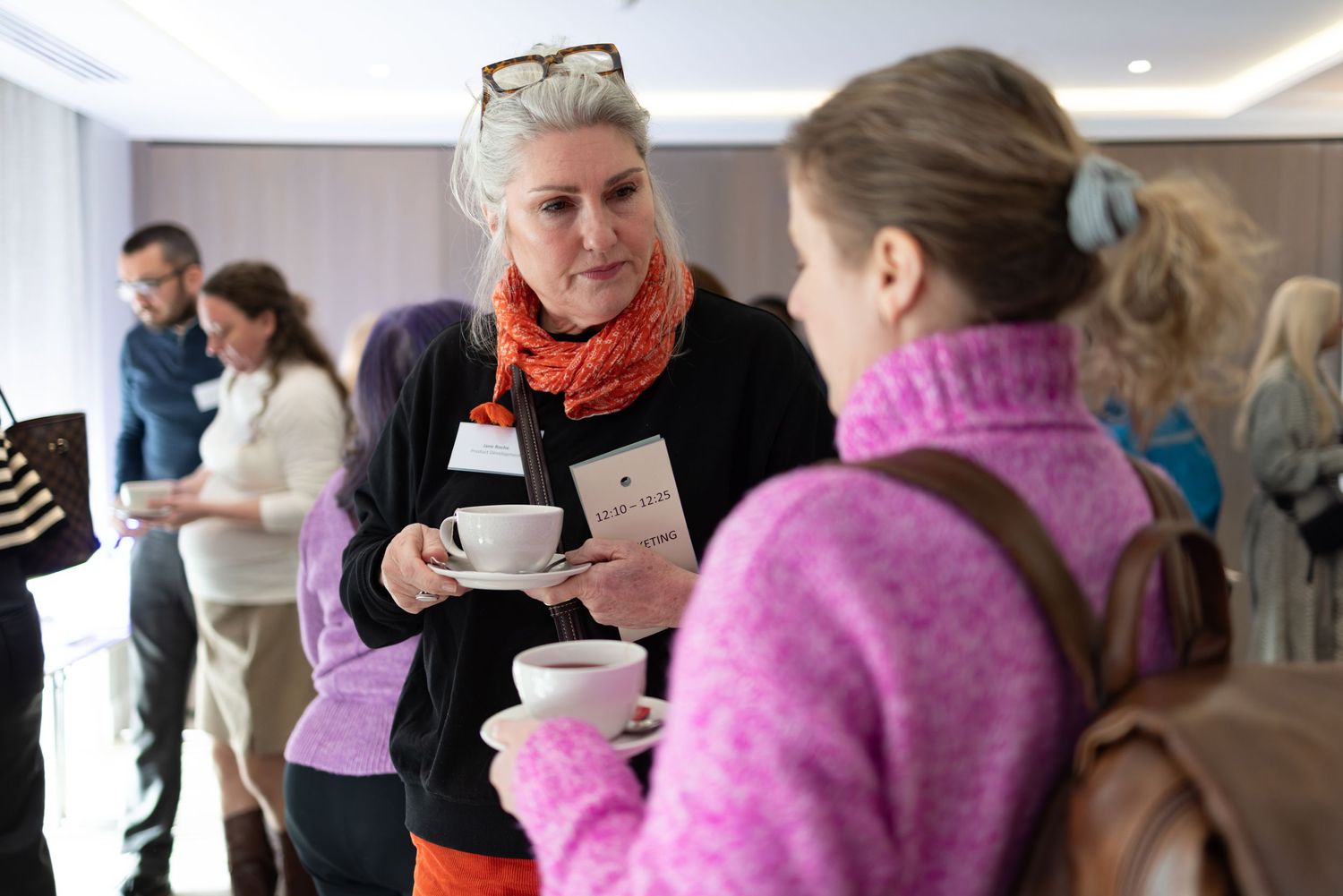 Two women chatting over tea at a corporate conference networking break, candid business networking photography