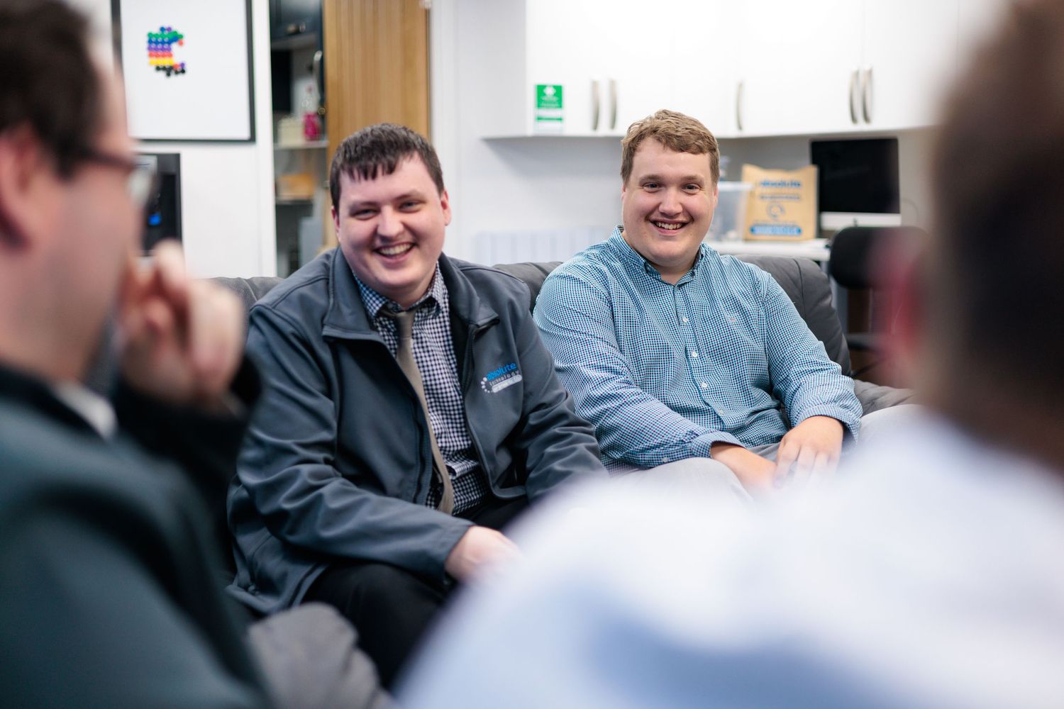 Two colleagues laughing together on a sofa in an office breakout area, candid corporate photography Southampton