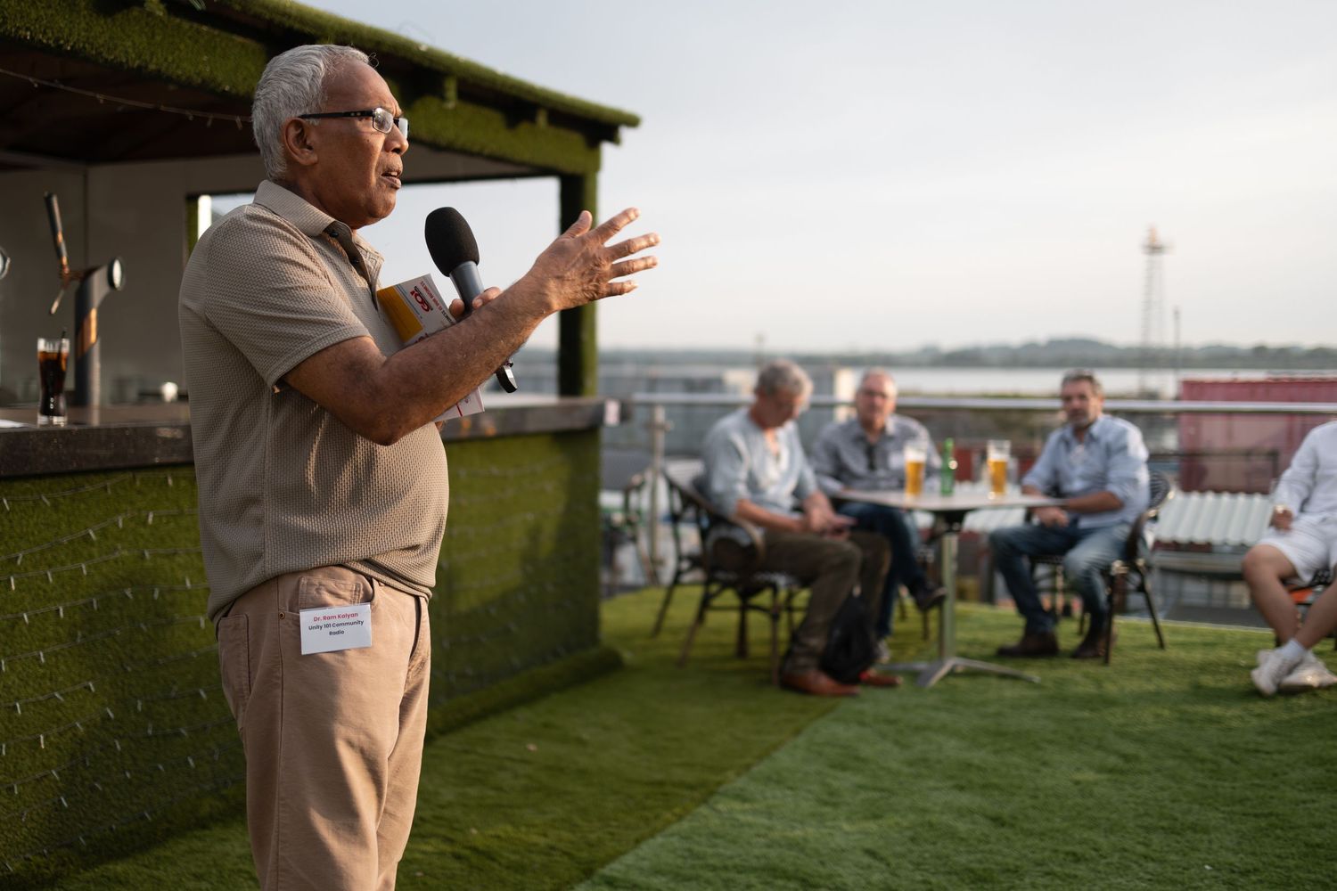 Speaker addressing guests with a microphone at a rooftop networking event with waterfront views, corporate event photography Southampton