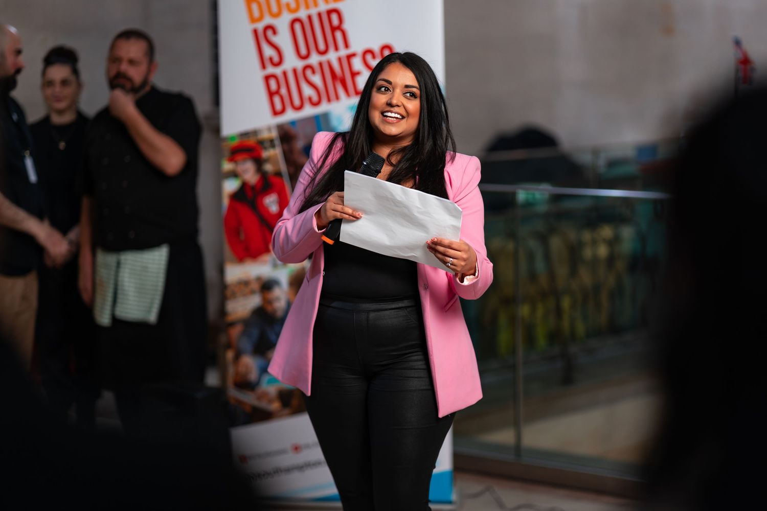Host in pink blazer speaking into a microphone and reading from notes at a business awards event, corporate awards event photography