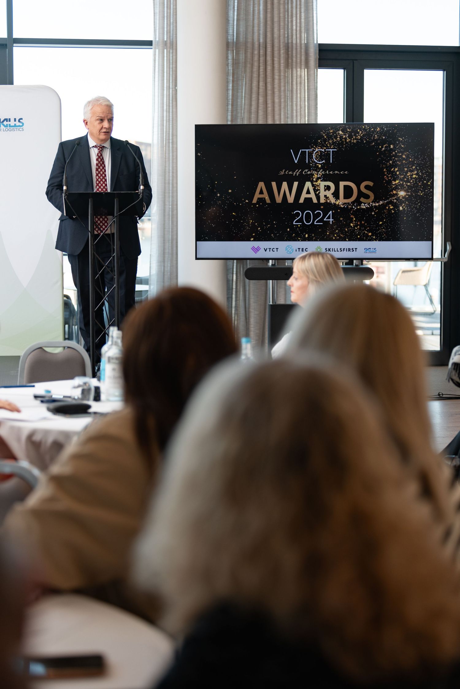 Speaker at podium presenting at the VTCT Staff Conference Awards 2024 with audience, corporate awards event photography