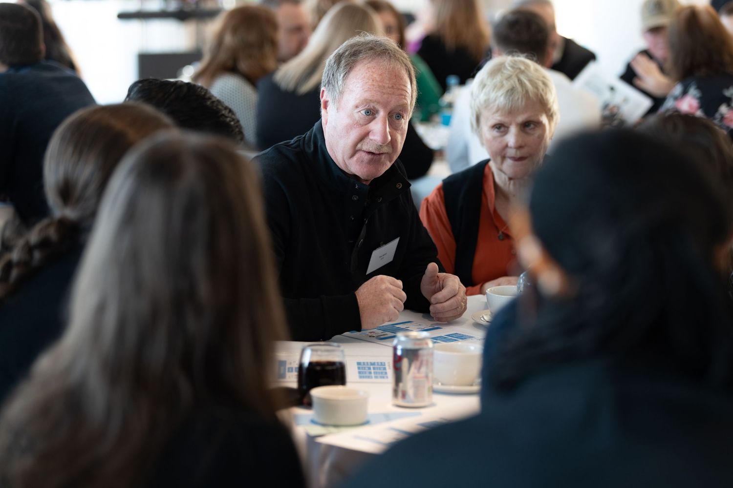 Delegates in conversation at a conference table with tea and coffee cups and printed materials, corporate conference photography Southampton