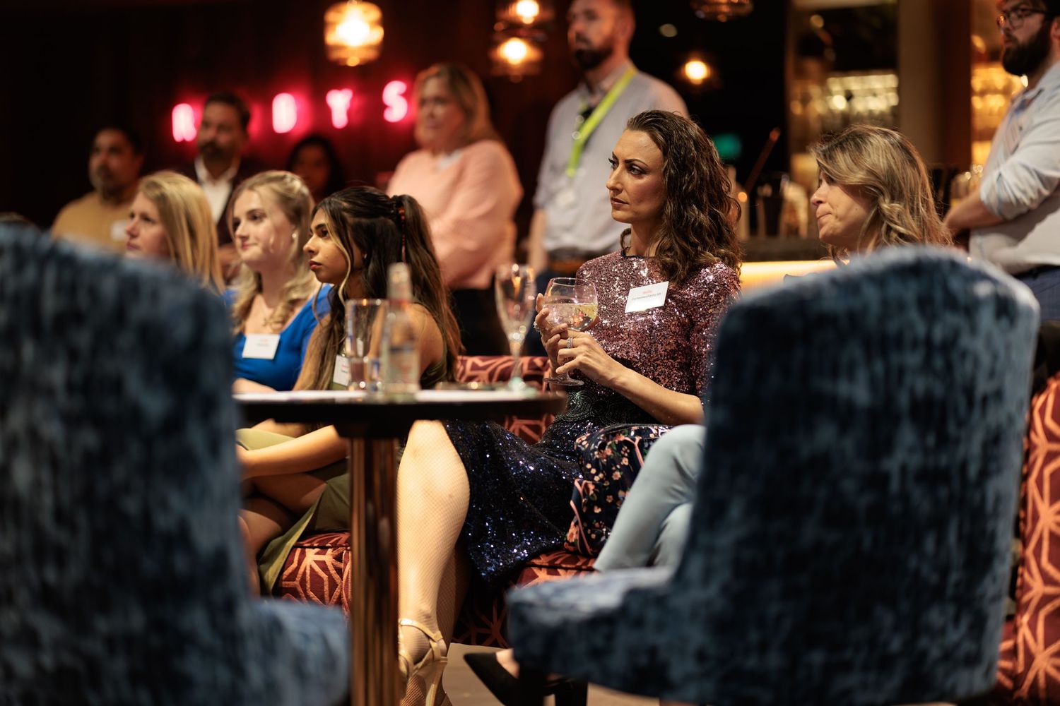 Guests seated with drinks at a corporate networking evening with Rubys neon signage in the background, corporate event photography