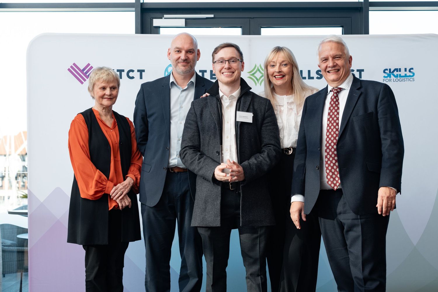 Group of five colleagues posing with a trophy in front of a VTCT branded backdrop at a staff conference awards, corporate awards event photography