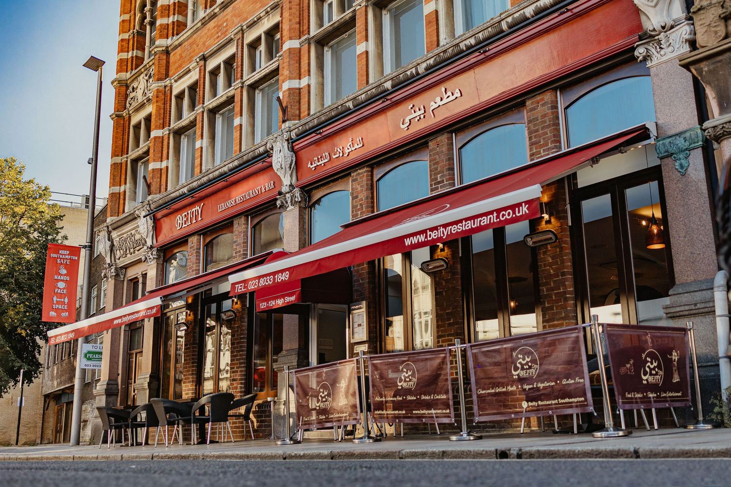 Beity Lebanese restaurant and bar exterior with red awnings, Arabic signage, arched windows, outdoor seating barriers and ornate Victorian building facade, commercial exterior photography