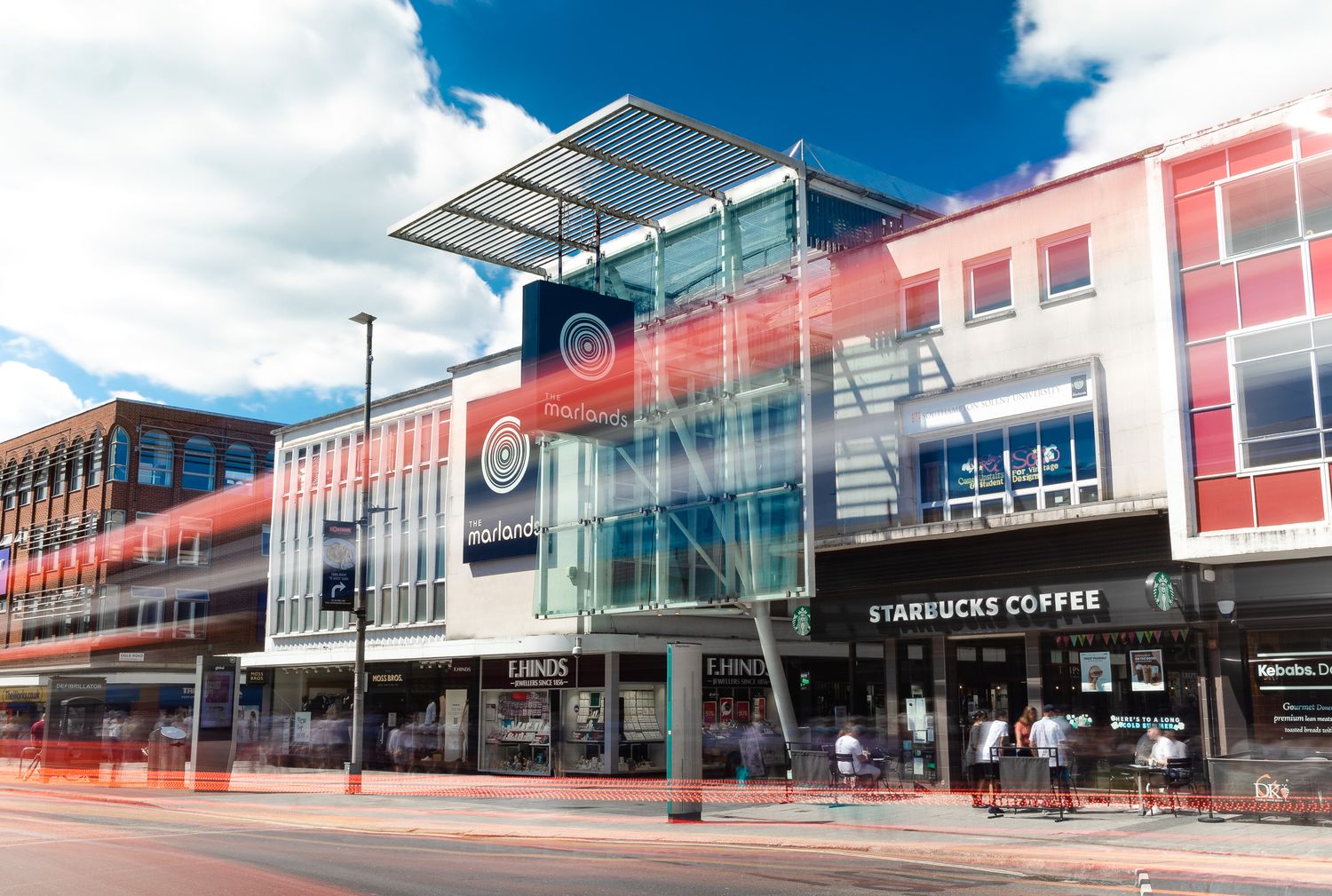 The Marlands shopping centre Southampton with glass and steel canopy, long-exposure motion blur of red bus and pedestrians, Starbucks Coffee and F.Hinds shopfronts, architectural exterior photography