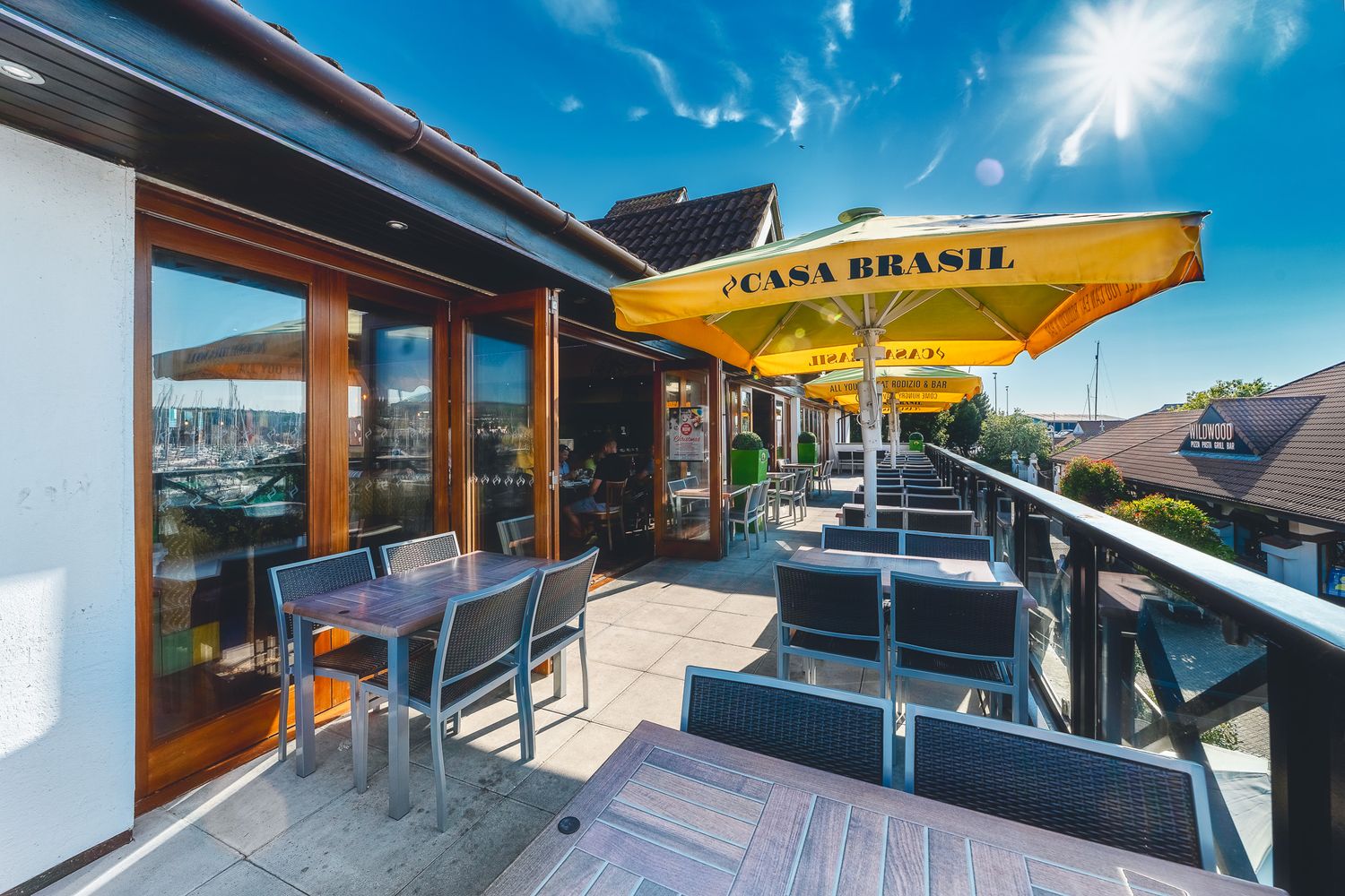 Casa Brasil Portsmouth terrace exterior with outdoor seating, yellow branded parasol, marina views and blue sky, commercial exterior photography