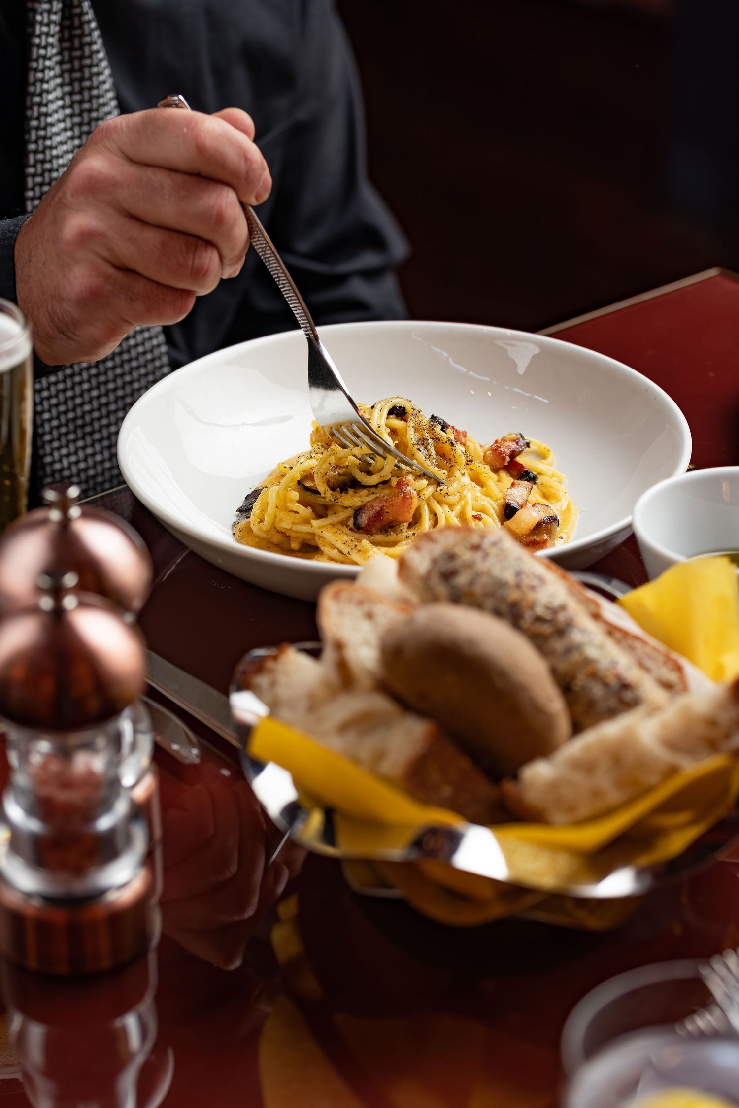 Diner twirling spaghetti carbonara with a bread basket in the foreground at an Italian restaurant, candid food photography Southampton