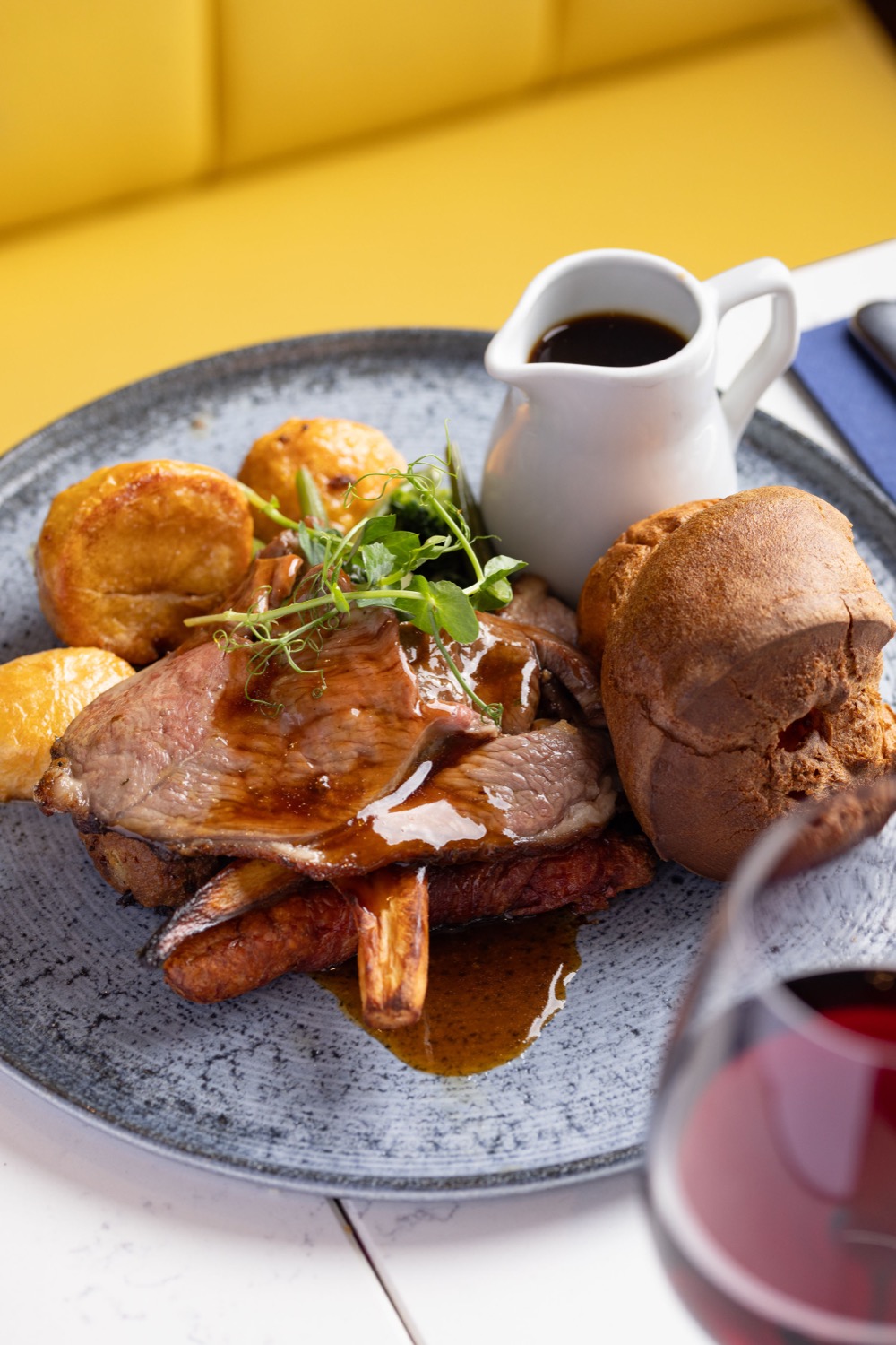 Sunday roast with sliced beef, Yorkshire puddings, roast potatoes and gravy jug on a grey plate at Banana Wharf Southampton, food photography