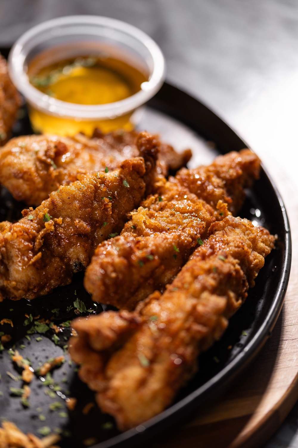 Crispy fried chicken strips with herbs and mustard dipping sauce on a black plate at Barga Eastleigh, food photography