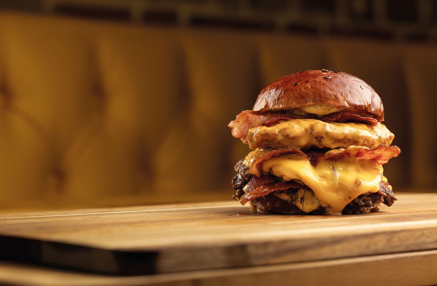 Stacked double smash burger with melted cheese and bacon on a pretzel bun on a wooden board in warm moody lighting at Kwackers, street food burger photography