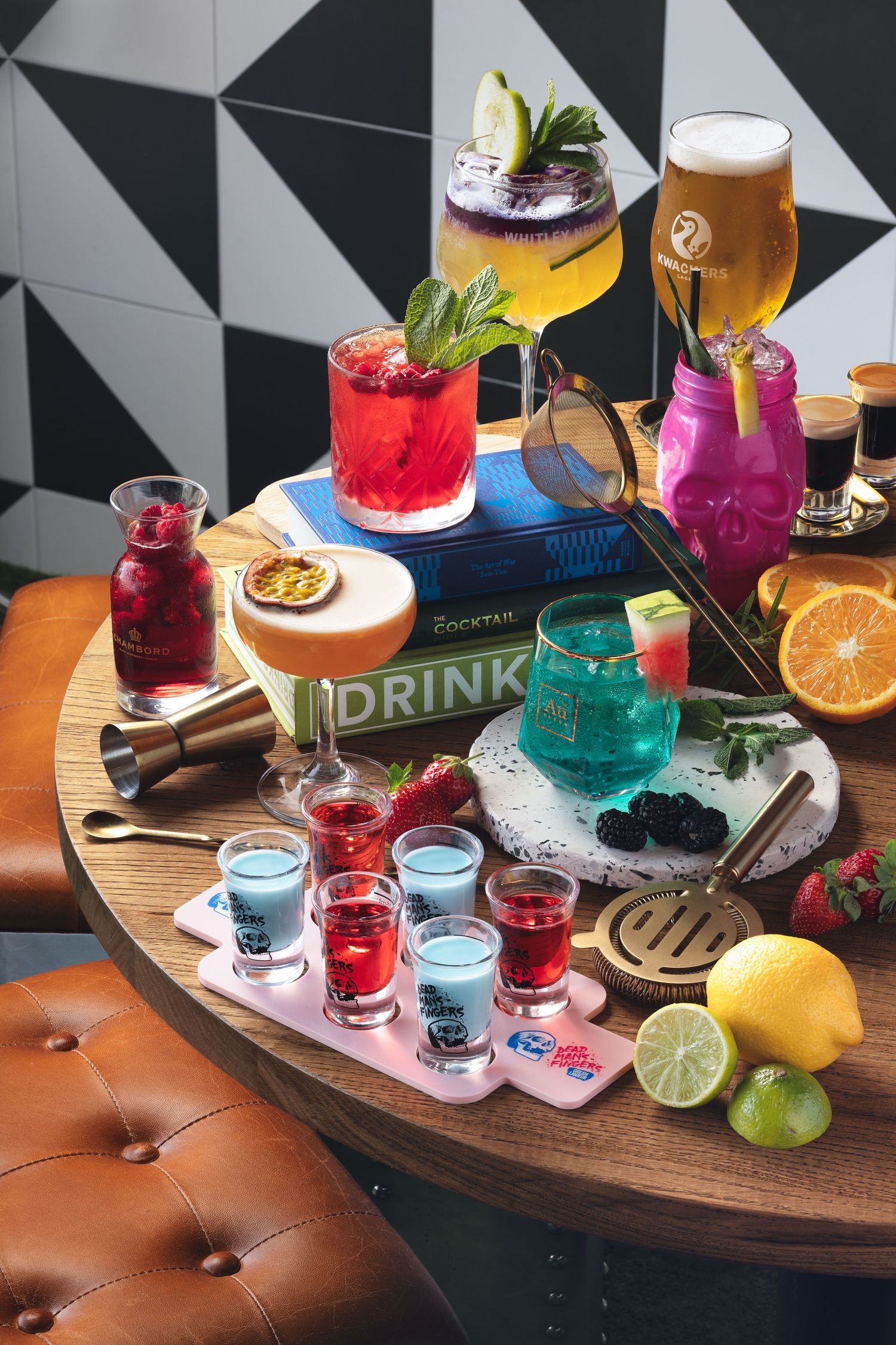 Colourful cocktail flatlay with shots, beer, mixed drinks, citrus garnishes and bar tools on a round wooden table, bar drinks menu photography Southampton
