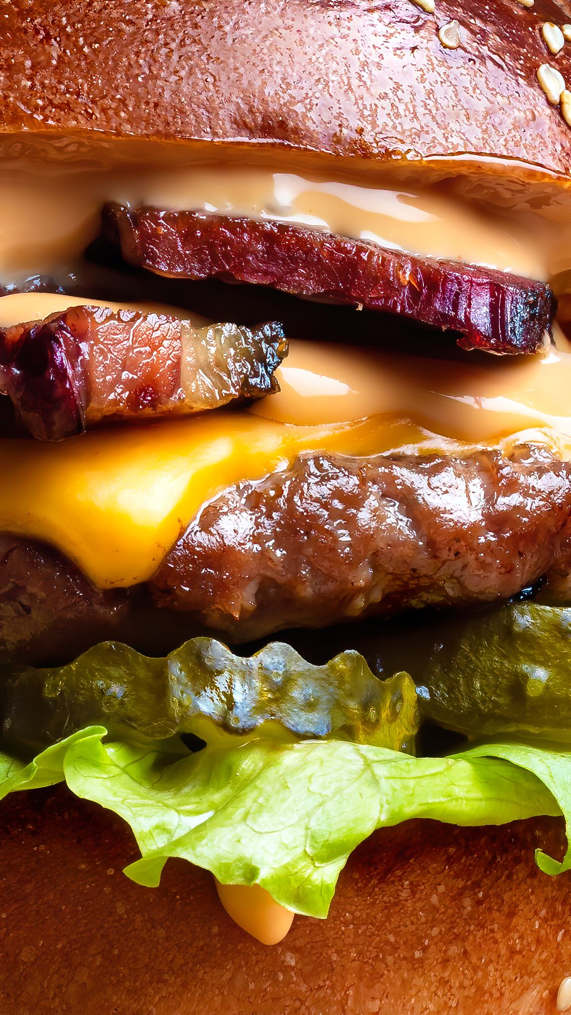 Close-up macro shot of a loaded bacon cheeseburger with melted cheese, pickles and lettuce on a brioche bun, street food burger photography