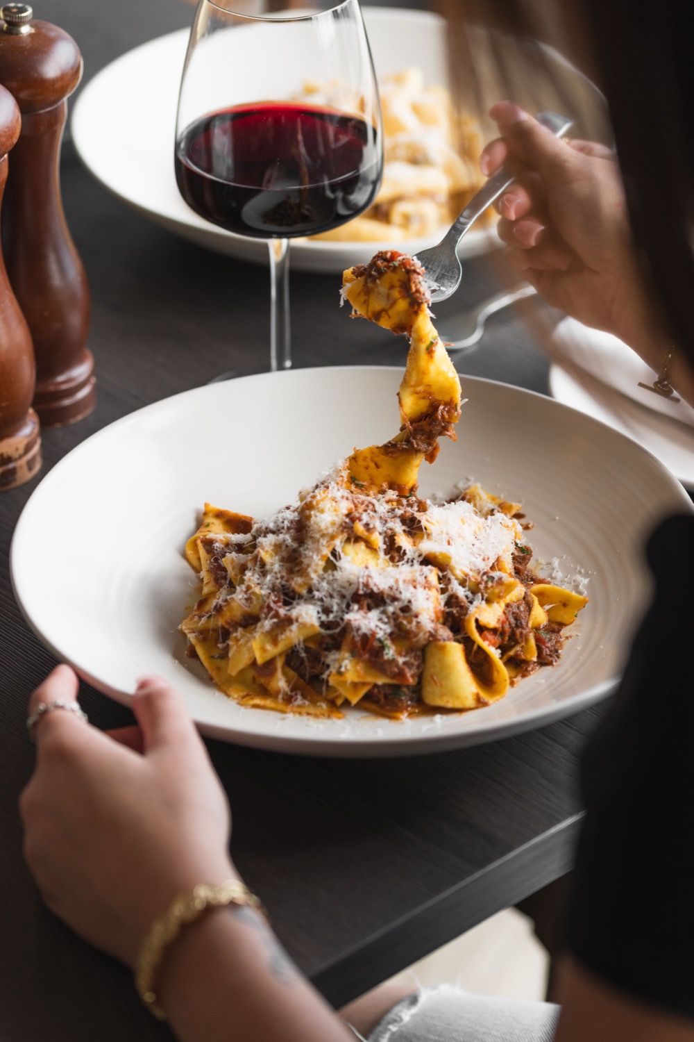 Pappardelle ragu being lifted on a fork with red wine glass in the background at Figurati Italian restaurant Southampton, lifestyle food photography