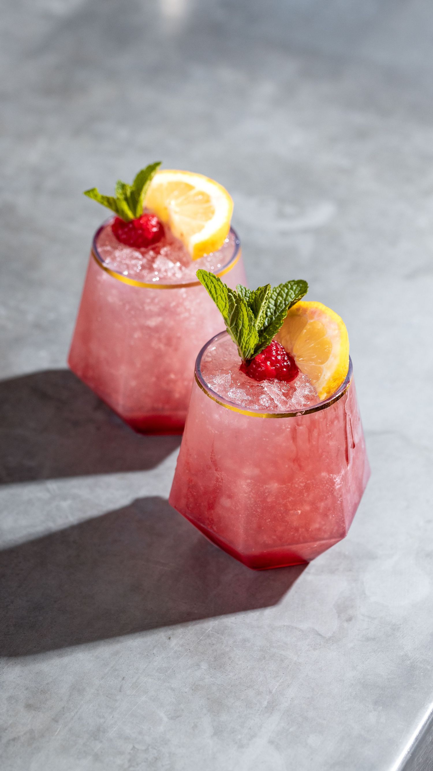 Pink raspberry lemonade cocktails with fresh mint and lemon garnish in geometric glasses, drink photography Southampton