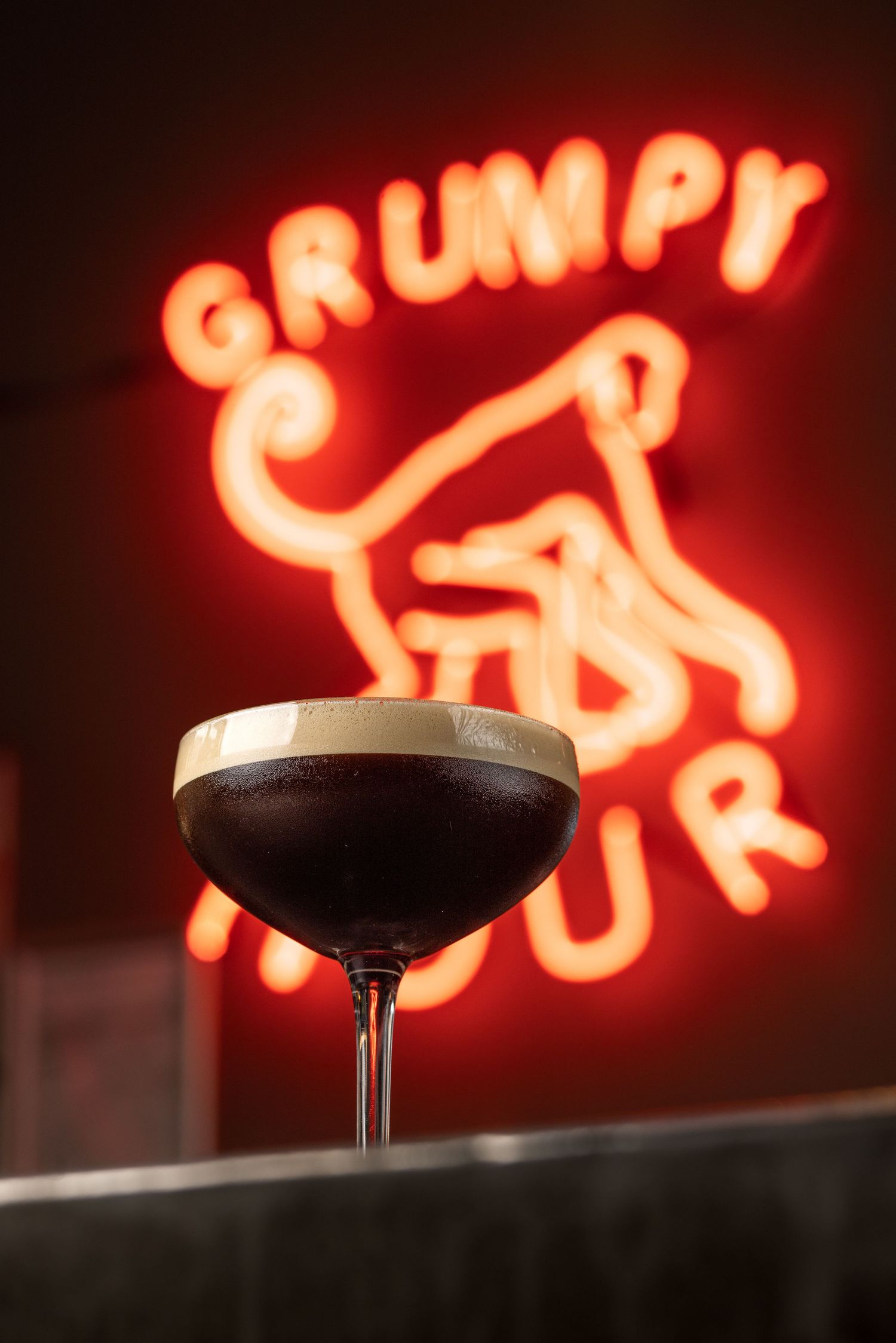 Espresso martini cocktail in a coupe glass with the red Grumpy Monkey neon sign at Grumpy Monkey bar Southampton, cocktail photography