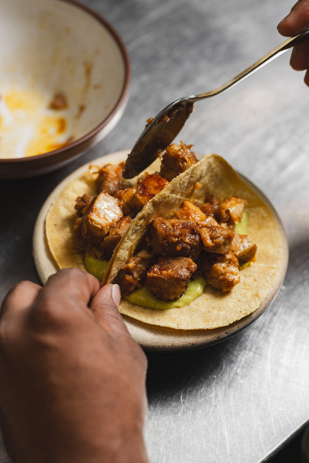 Slow-cooked pork tacos on soft corn tortillas being spooned over guacamole at Ixchel Mexican restaurant on the King's Road, Chelsea, London food photography