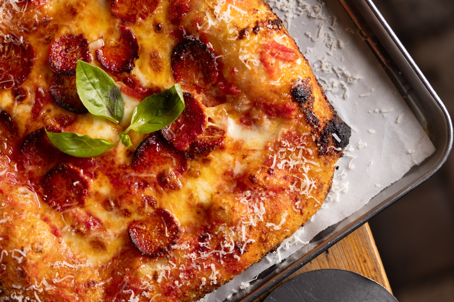 Pepperoni pizza with basil and grated parmesan in a baking tray at Made in Italy