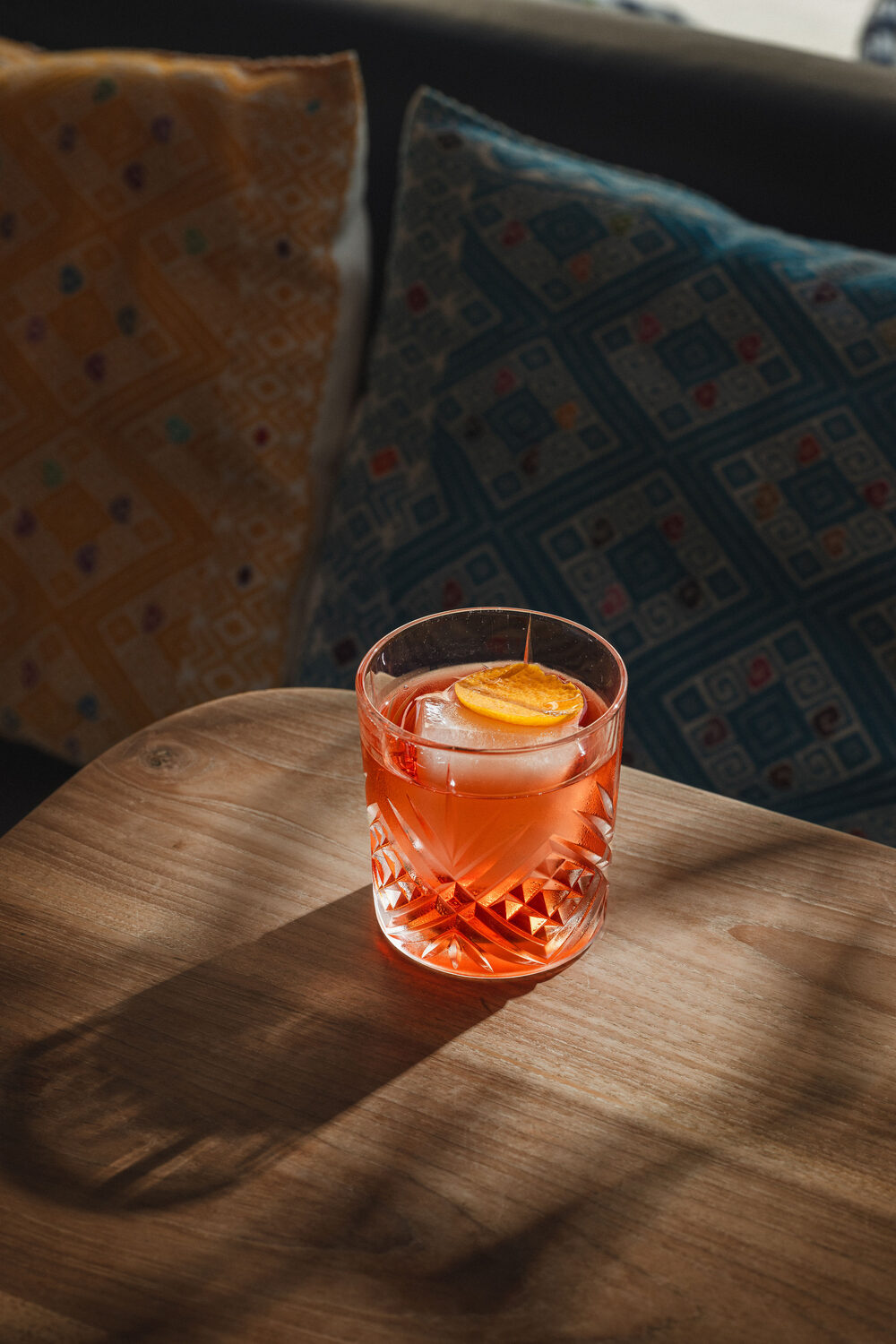 Negroni style cocktail with an orange twist on a wooden table beside patterned cushions at Mestizo Mexican restaurant, King's Road Chelsea, London drink photography