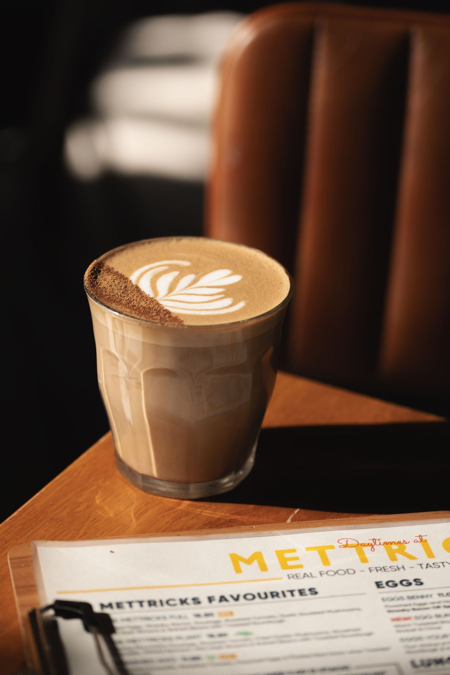 Latte with latte art in a glass tumbler on a wooden table with the Mettricks menu at Mettricks Portswood cafe Southampton, coffee photography
