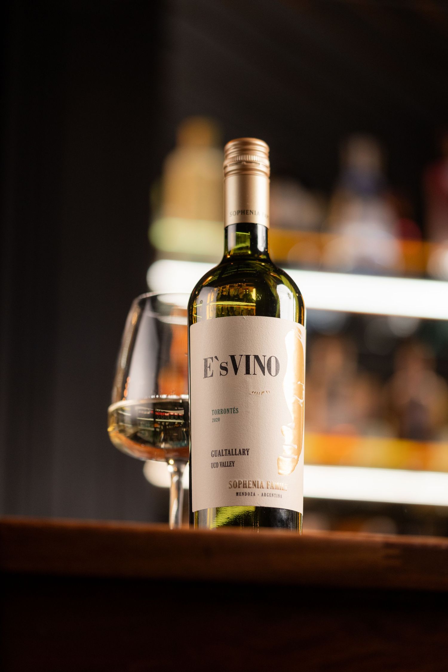 Bottle of E'sVINO Torrontes white wine with a poured glass on a bar top with warm bokeh lighting at Porters Southampton, wine photography