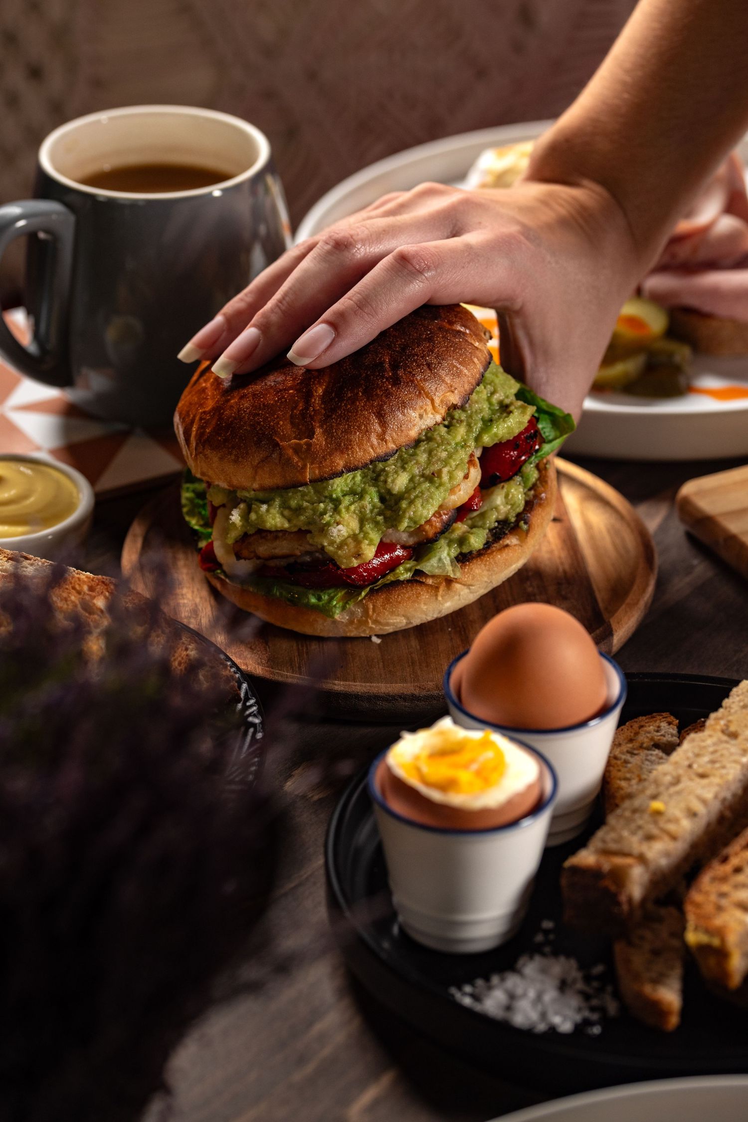 Brunch spread with a guacamole and roasted pepper brioche burger, soft-boiled eggs in egg cups with toast soldiers and coffee at Room2 cafe, food photography Southampton