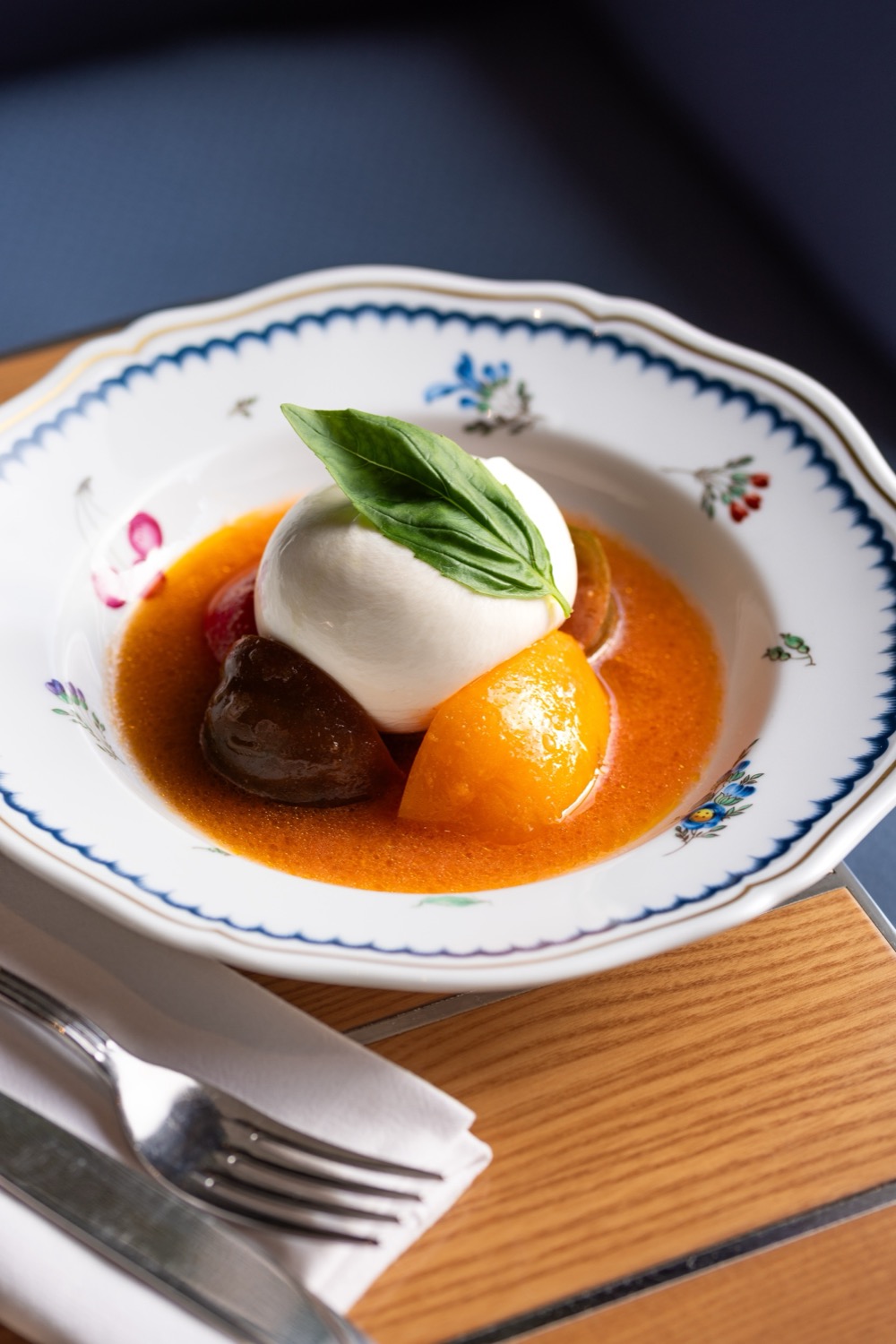 Burrata with heritage tomatoes and basil leaf in tomato sauce on a floral-patterned china plate at Alba Knightsbridge, Italian food photography London
