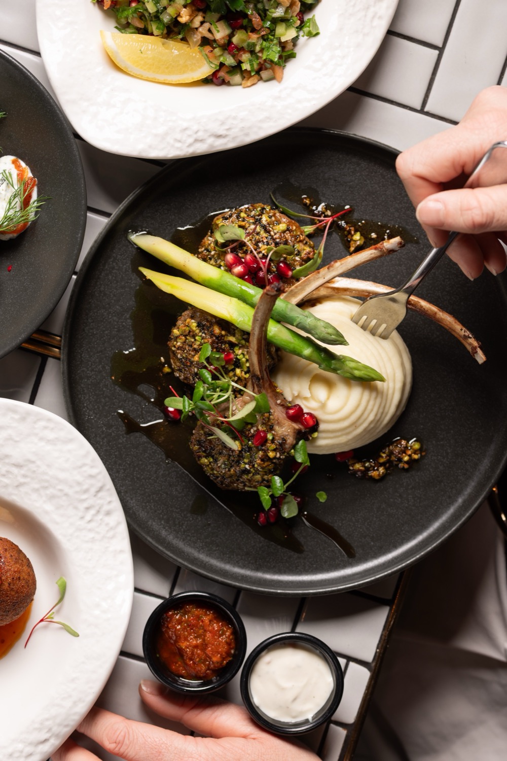 Pistachio-crusted lamb cutlets with asparagus, cauliflower puree, pomegranate seeds and balsamic reduction on a dark plate at The Mantl Knightsbridge, Turkish food photography London