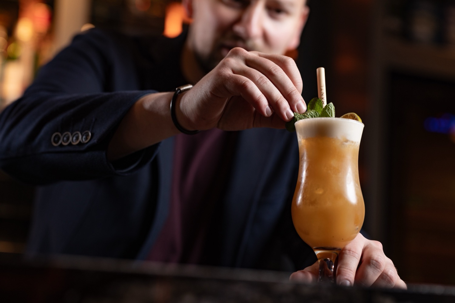 Bartender garnishing a tropical cocktail with mint and a paper straw in a hurricane glass at The Mantl Knightsbridge, cocktail photography London