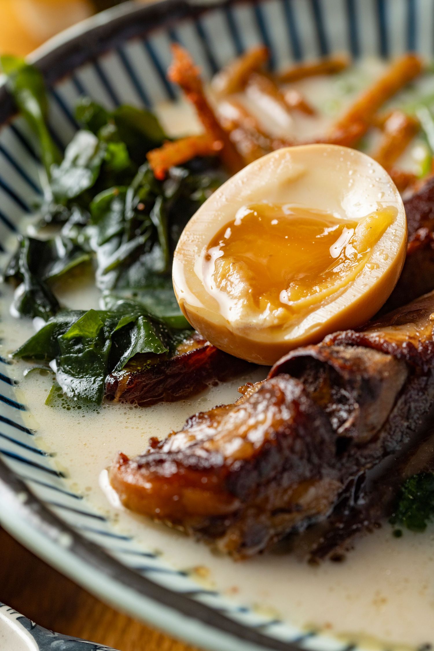 Close-up of braised pork belly chashu with a soft-boiled ramen egg, wilted greens and crispy enoki in a creamy broth at Sakura Japanese restaurant, food photography