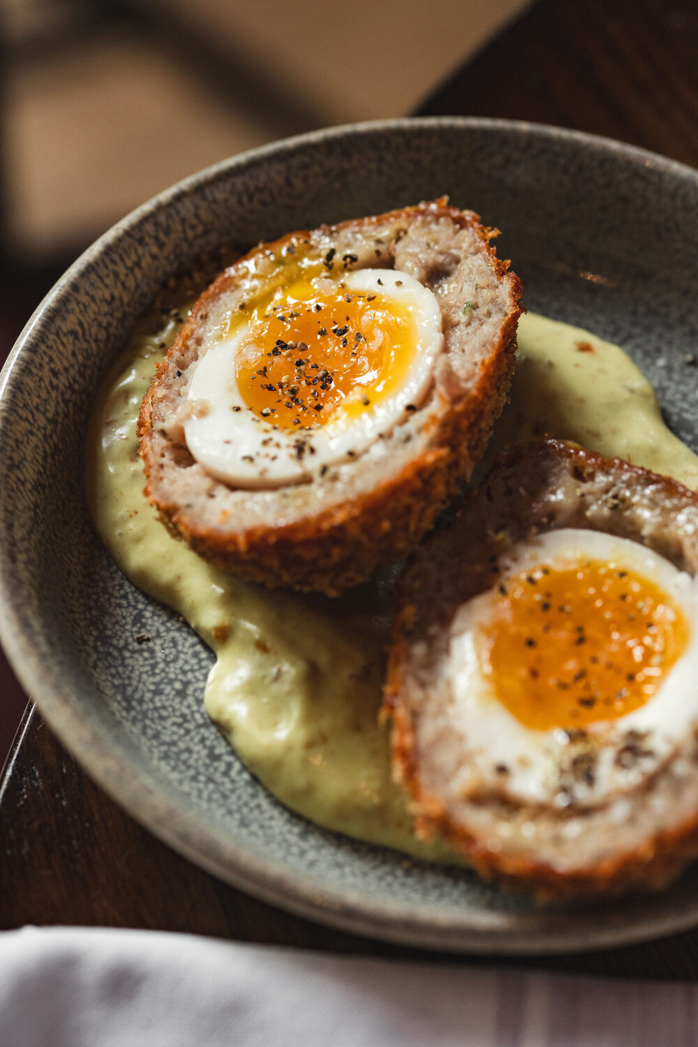 Halved scotch eggs with runny yolks on a herb and pea puree in a stone bowl at The Trafalgar Chelsea, new menu food photography London