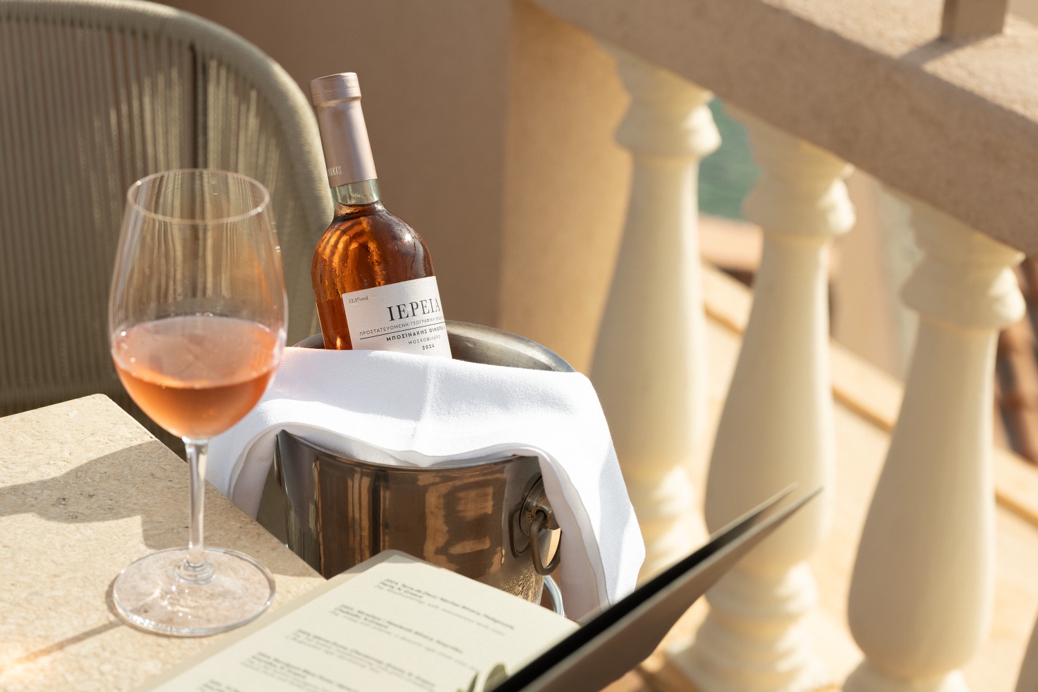 Chilled rose in an ice bucket beside a filled glass and an open menu on a stone balustrade terrace, Casa Delfino rooftop bar, Chania, Crete, drinks photography