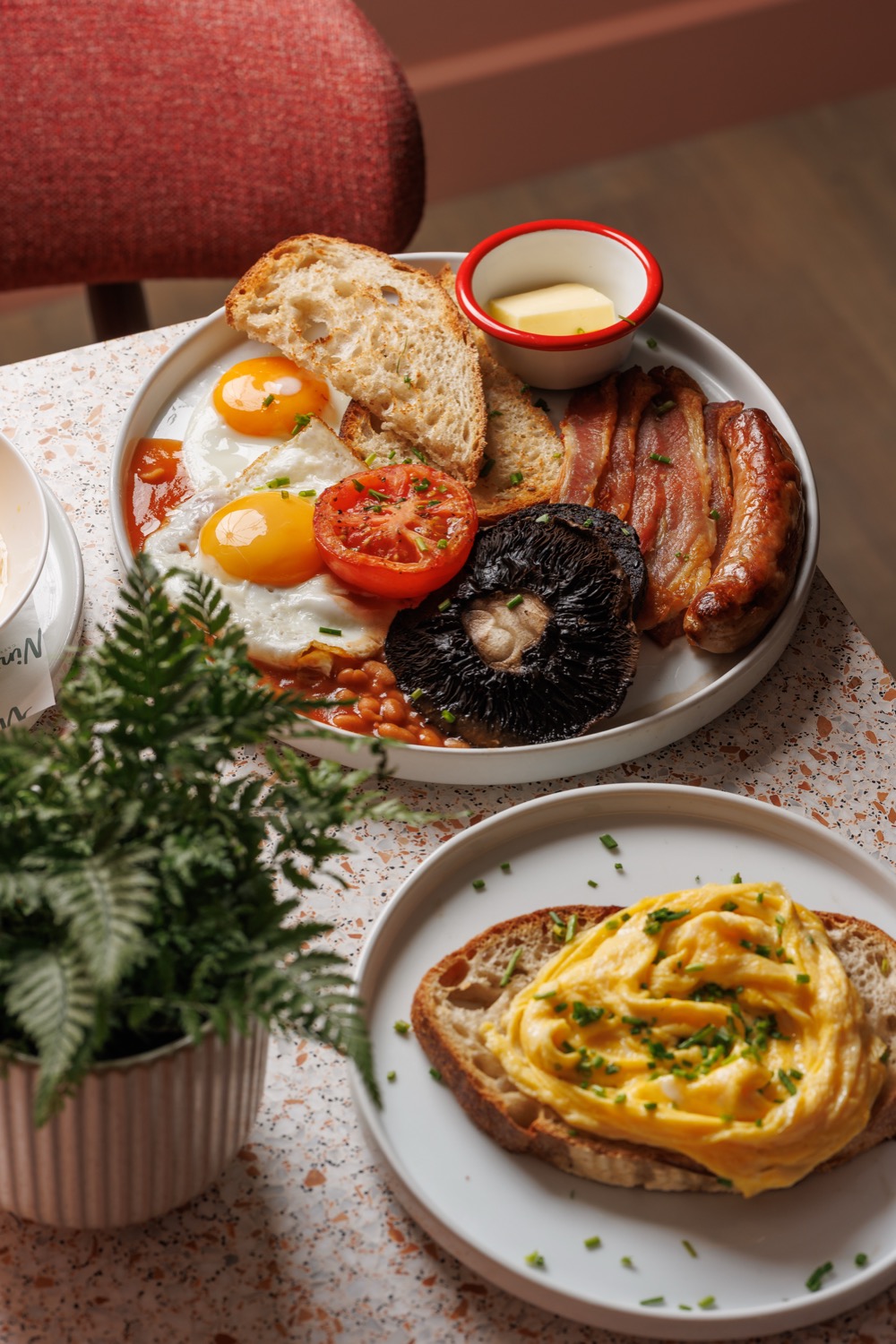 Full English breakfast with fried eggs, bacon, sausage, roast tomato, flat mushroom, beans and sourdough toast beside scrambled eggs on toast, on a terrazzo table, Second Nature, Southampton, food photography