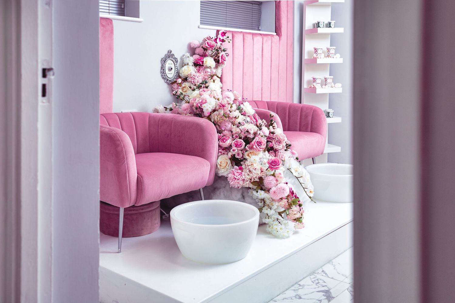 Glam Salon pedicure area with pink velvet tub chairs, cascading floral arrangement, white pedicure bowls and pink panelled wall, commercial salon interior photography