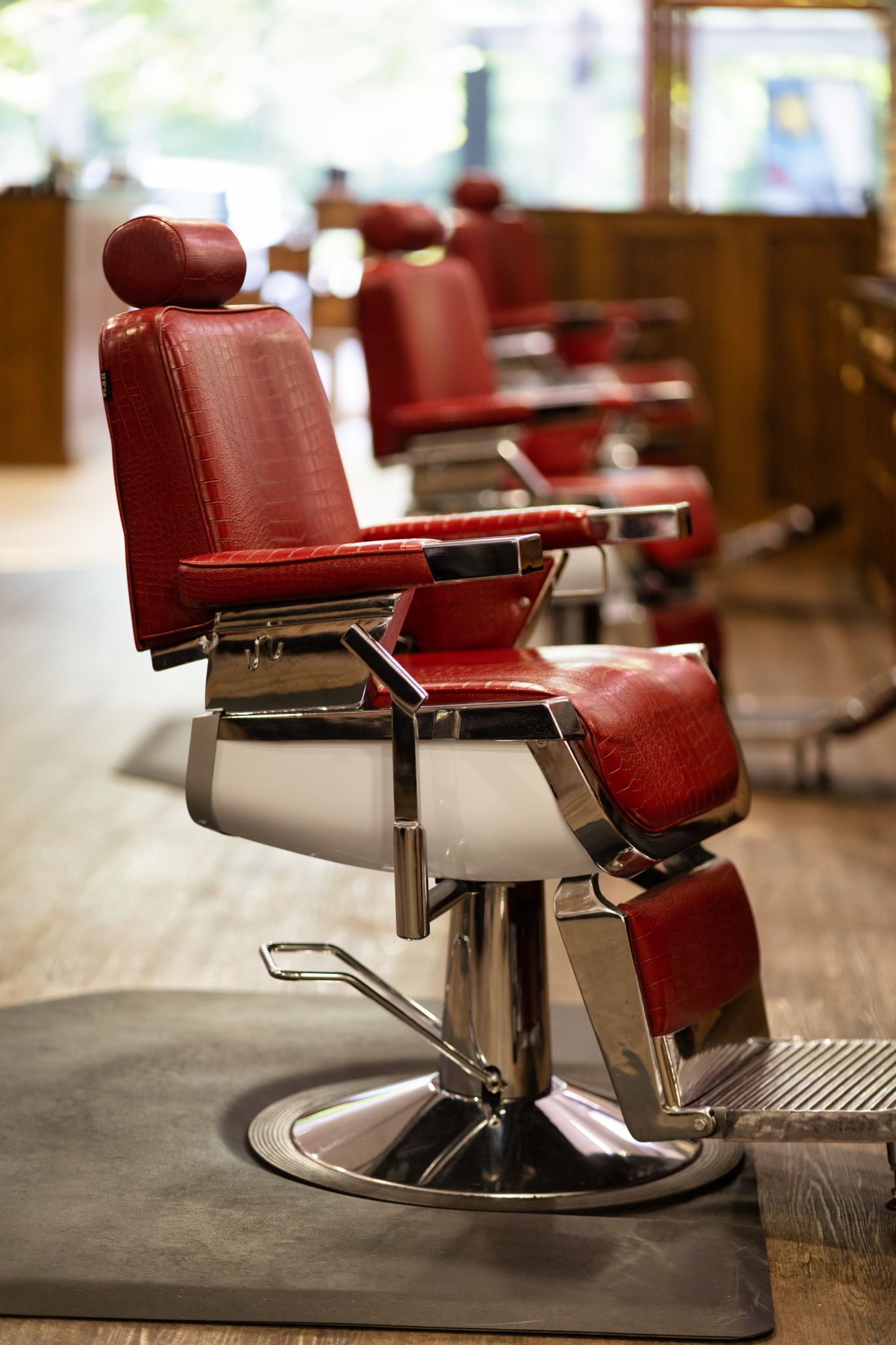 Row of red leather barber chairs with chrome bases on dark floor in a traditional barber shop with wooden panelling, commercial barber shop interior photography