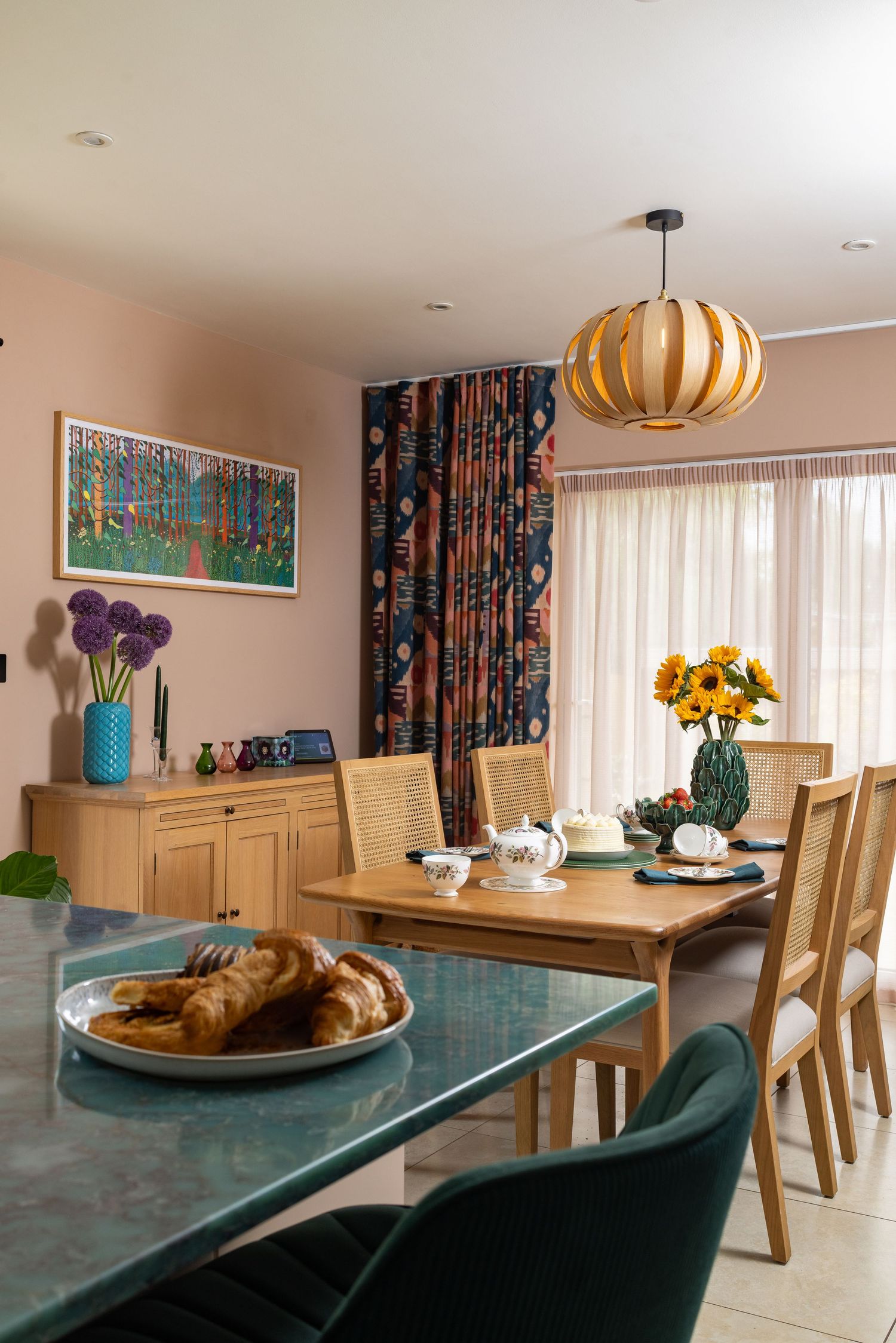 Modern kitchen with pink cabinets, white terrazzo worktops, purple stripe ceiling detail, green bar stools, trailing houseplant and wooden floor, kitchen interior photography