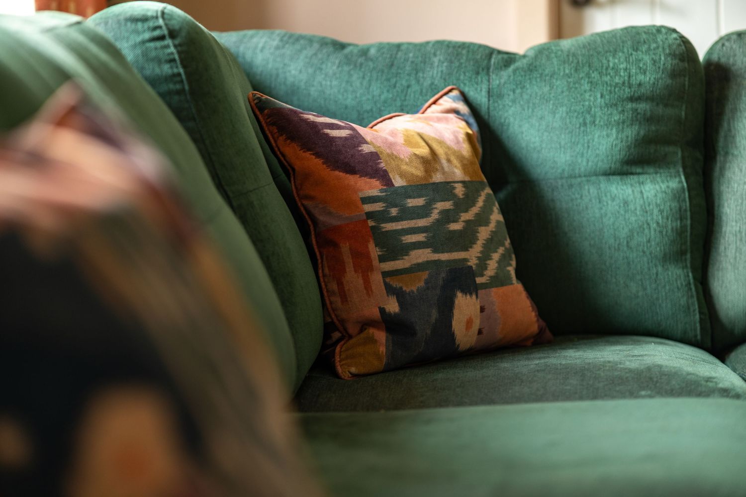 Close-up of teal green sofa with abstract patterned ikat cushion in warm tones, interior detail photography