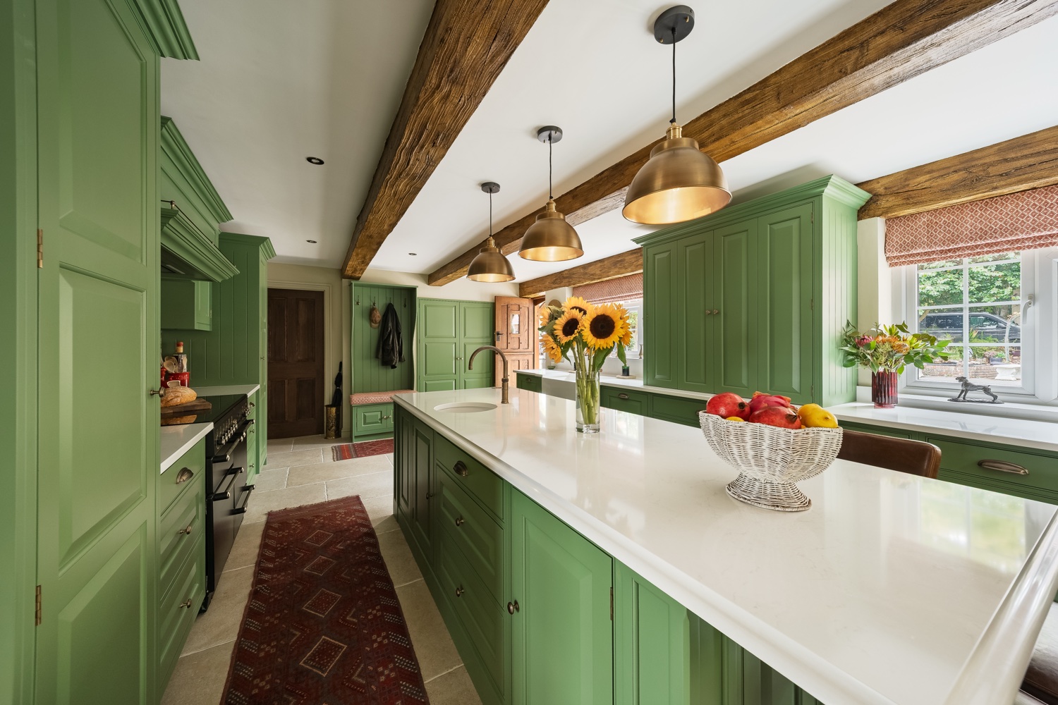 Farmhouse kitchen with sage green cabinetry, oak beams and brass pendant lights, for Leisha Norman Interior Design
