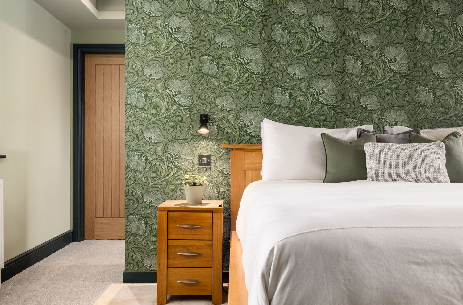 Bedroom with green floral wallpaper, oak bedside table and wall lamp, designed by Leisha Norman, photographed by Ryan Stanikk in Hampshire