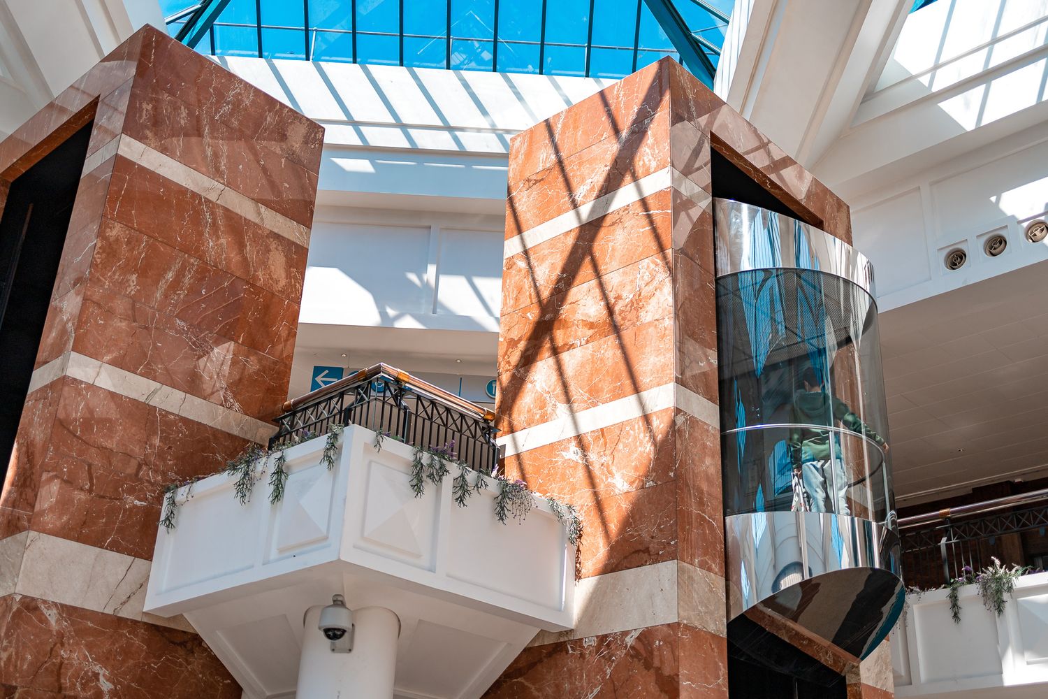 The Marlands shopping centre atrium interior with red marble columns, glass lift, glass skylight ceiling and decorative balcony, commercial architectural interior photography