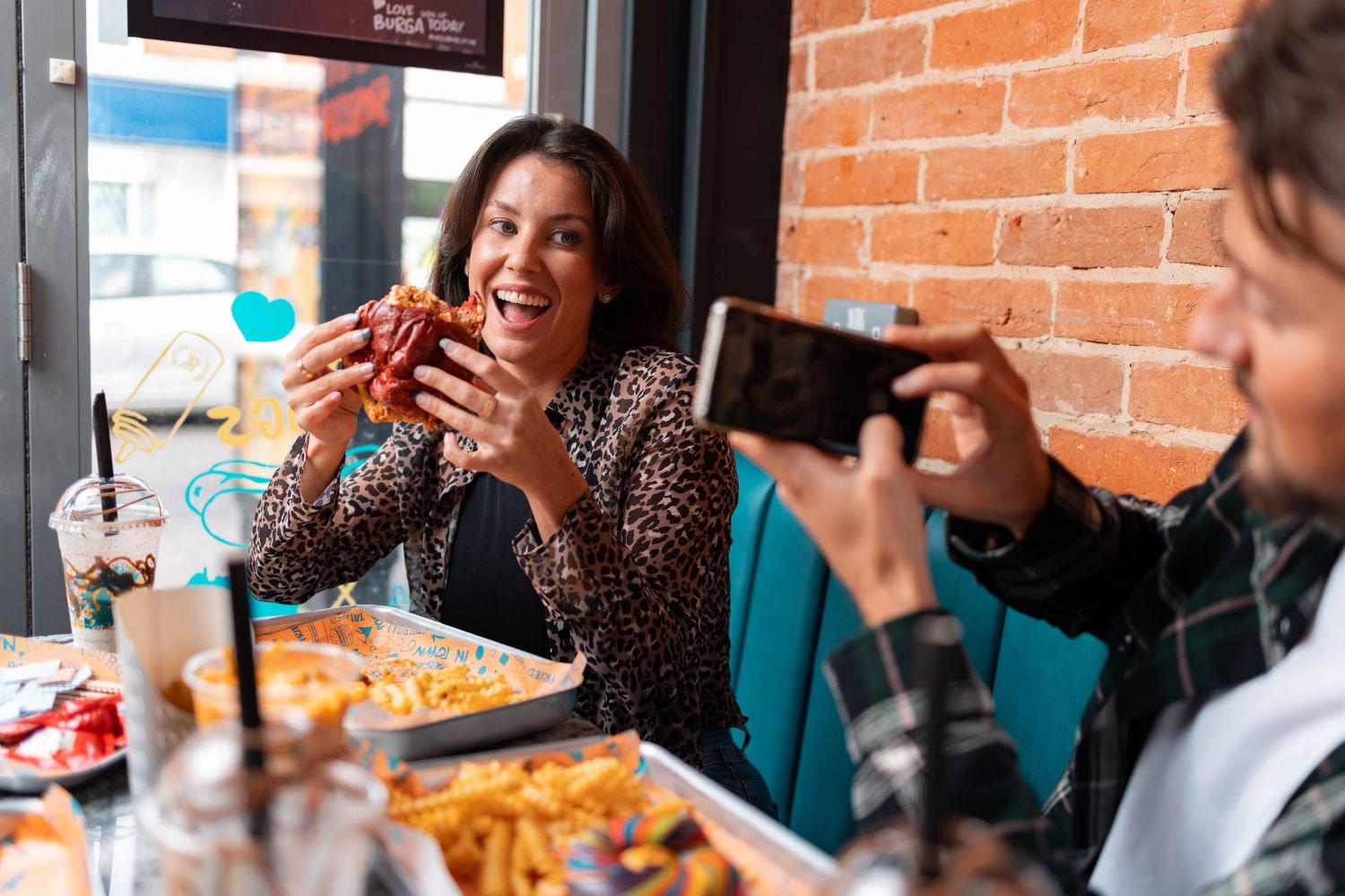 Woman holding up a burger and laughing while being photographed at Burga restaurant Portsmouth, candid dining lifestyle photography