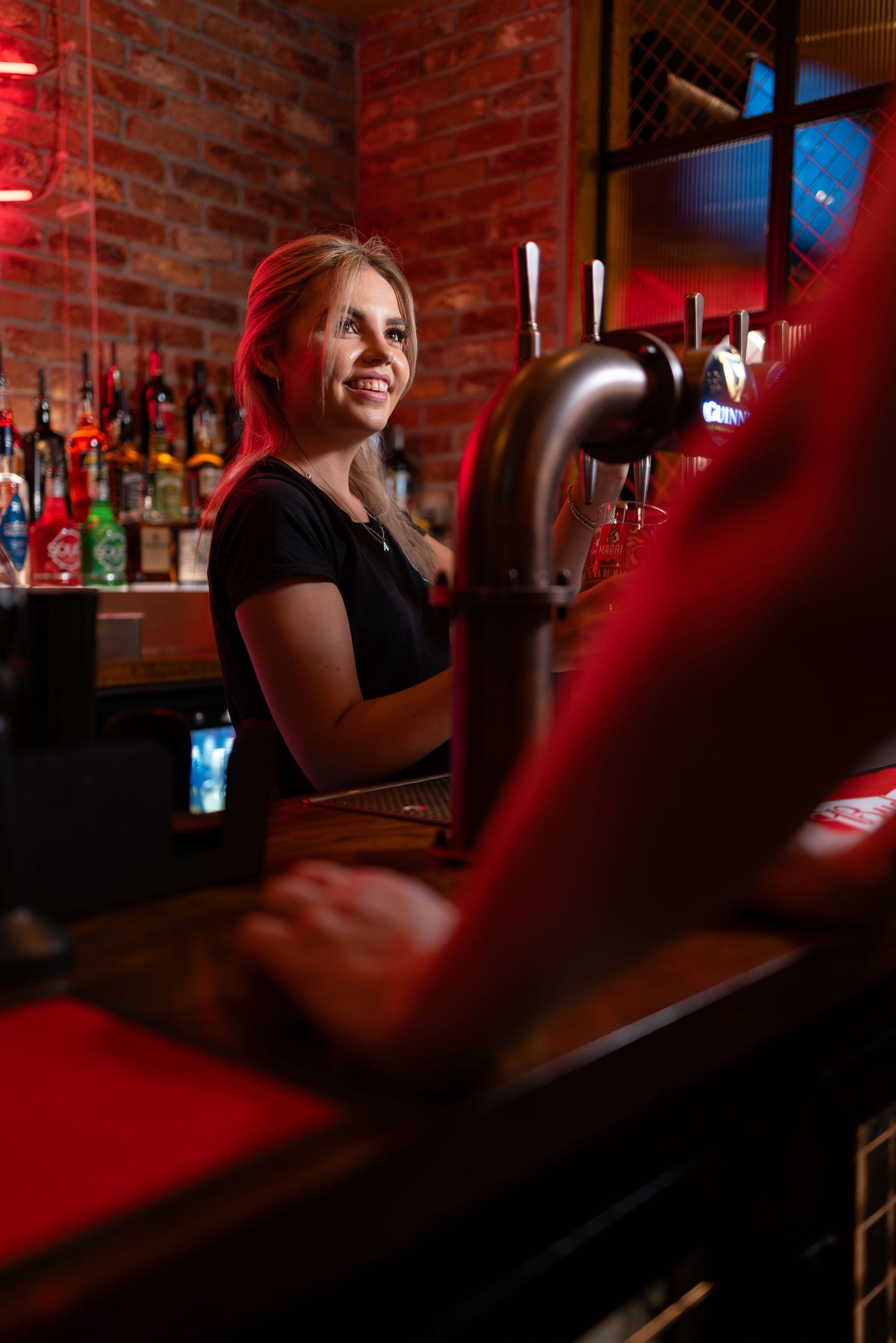 Smiling bartender behind the bar with beer taps and spirits at Arrowsmiths bar Southampton, hospitality lifestyle photography