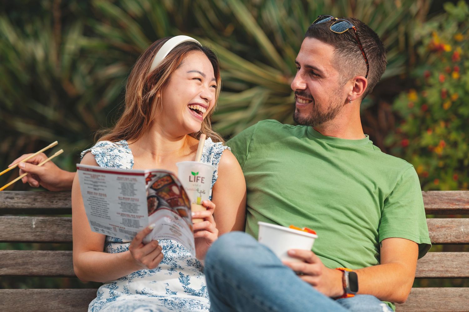 Couple laughing on a park bench with takeaway food and a menu for Co-Sushi Southampton, outdoor social lifestyle photography