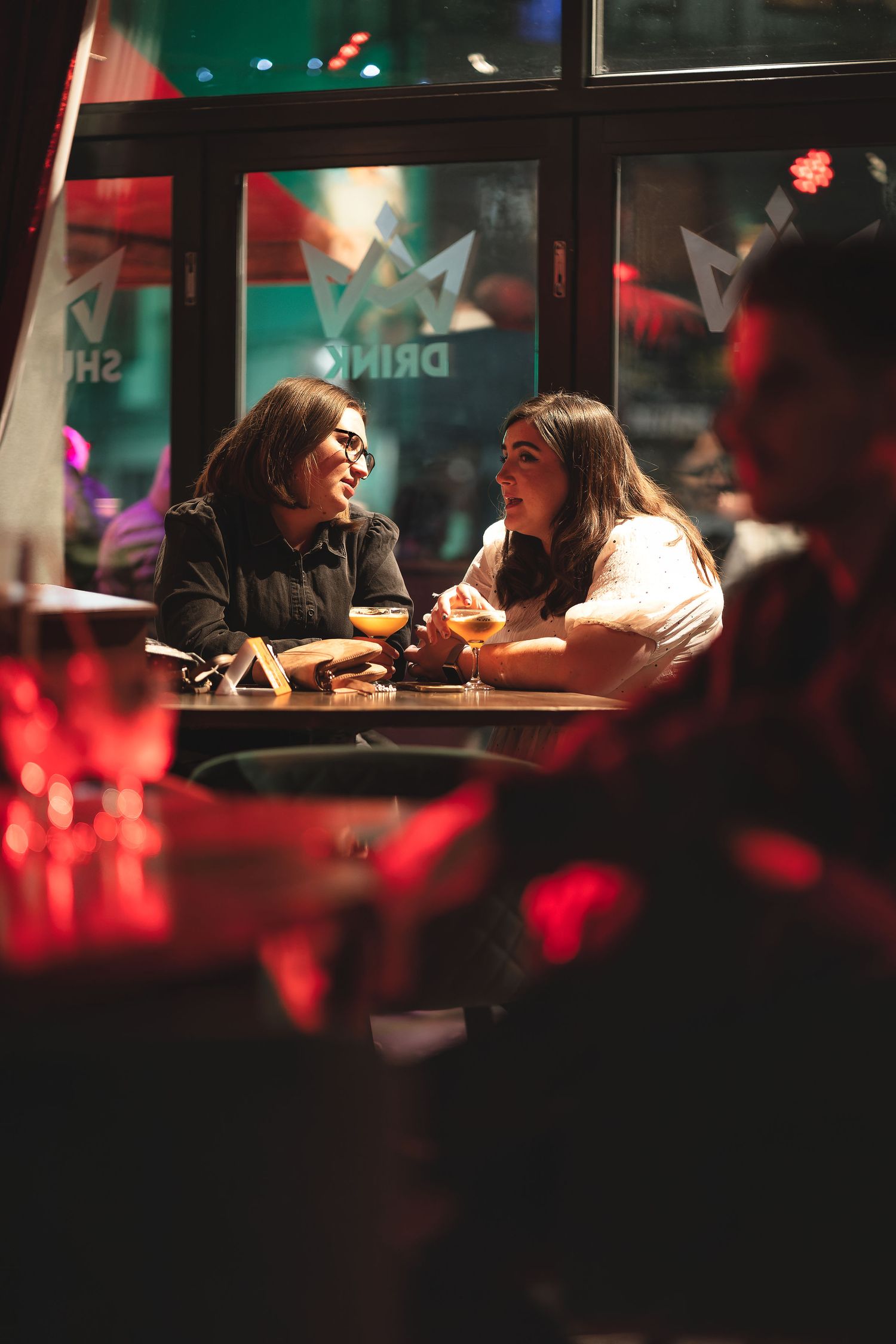 Two friends chatting over espresso martinis at a bar table with warm ambient lighting, candid nightlife lifestyle photography Southampton