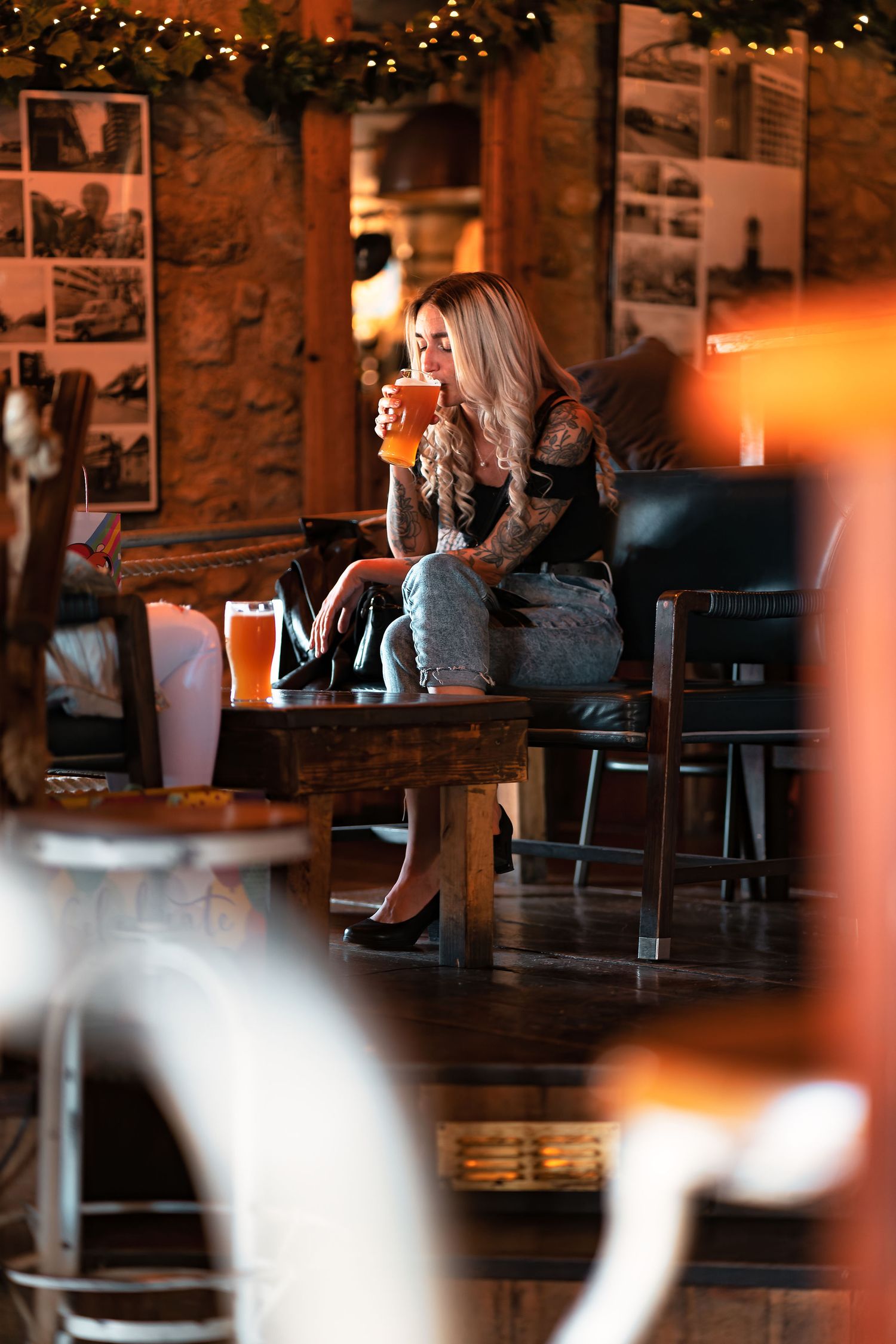 Woman sipping a pint of beer on a sofa at The Dancing Man brewery Southampton with fairy lights and photos on the walls, relaxed pub lifestyle photography